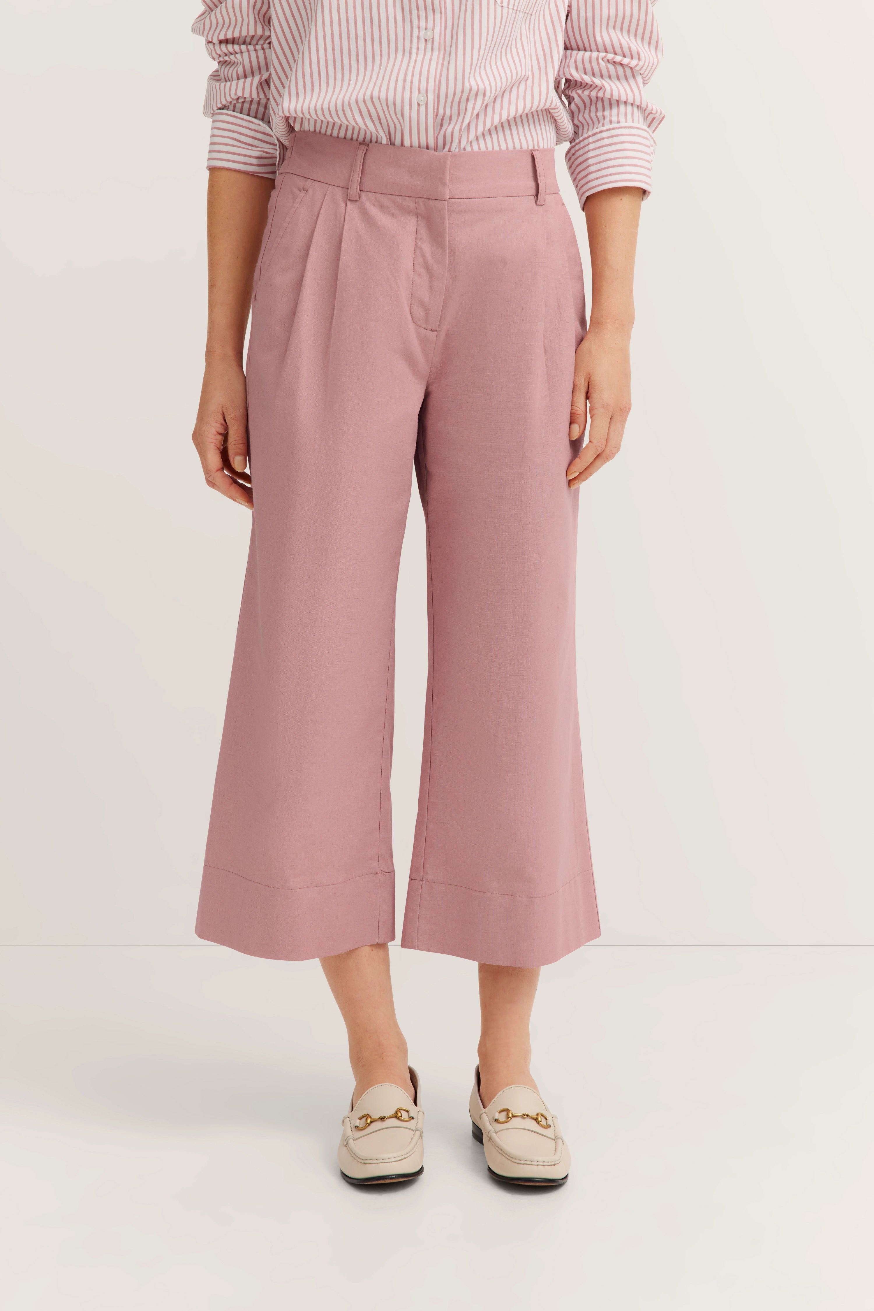Roze culotte-broek en gestreept shirt, casual modelbeeld, handen ontspannen aan de zijkant.