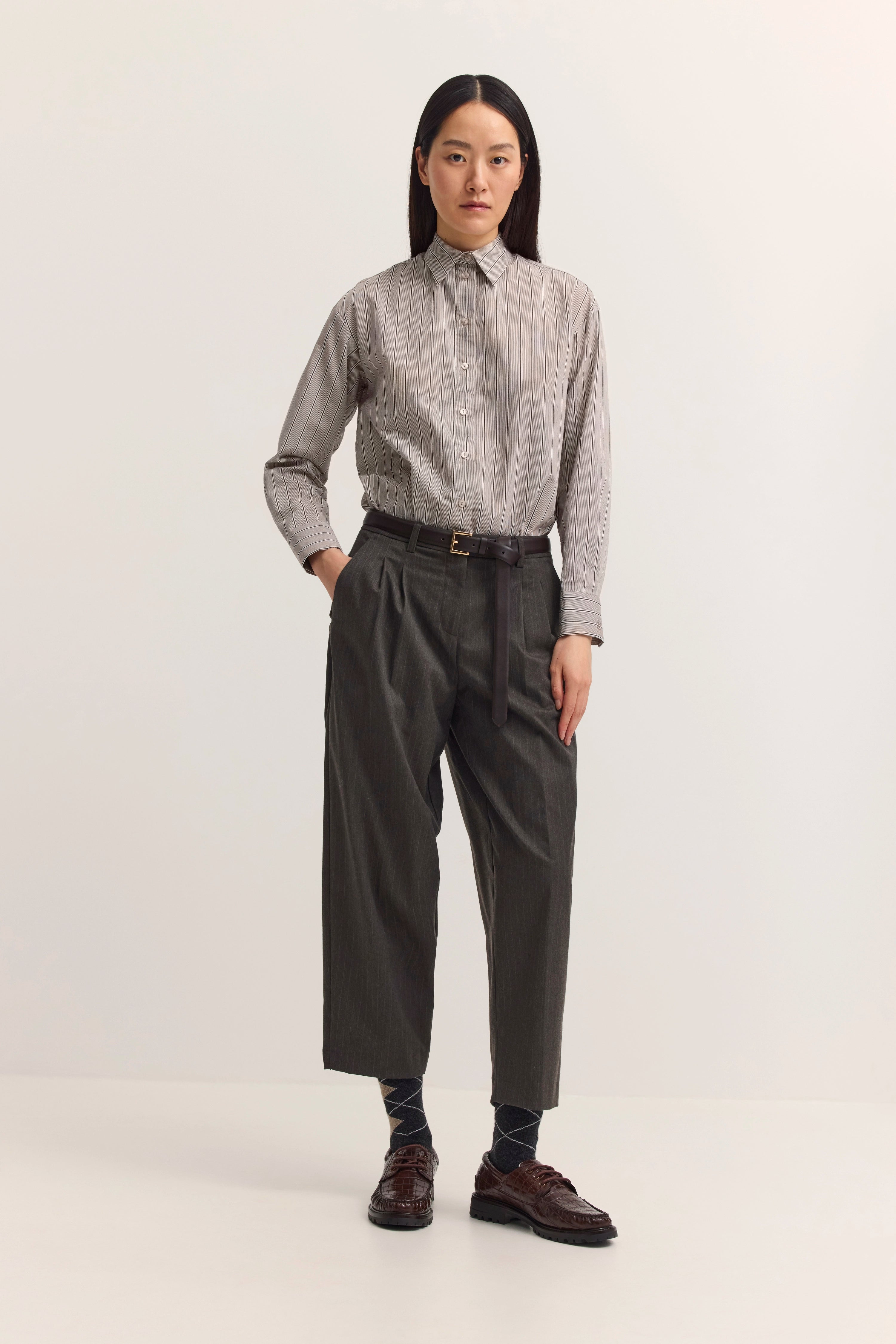 Graues gemustertes Hemd, graue Hose, Model steht aufrecht, Hände in den Hosentaschen.