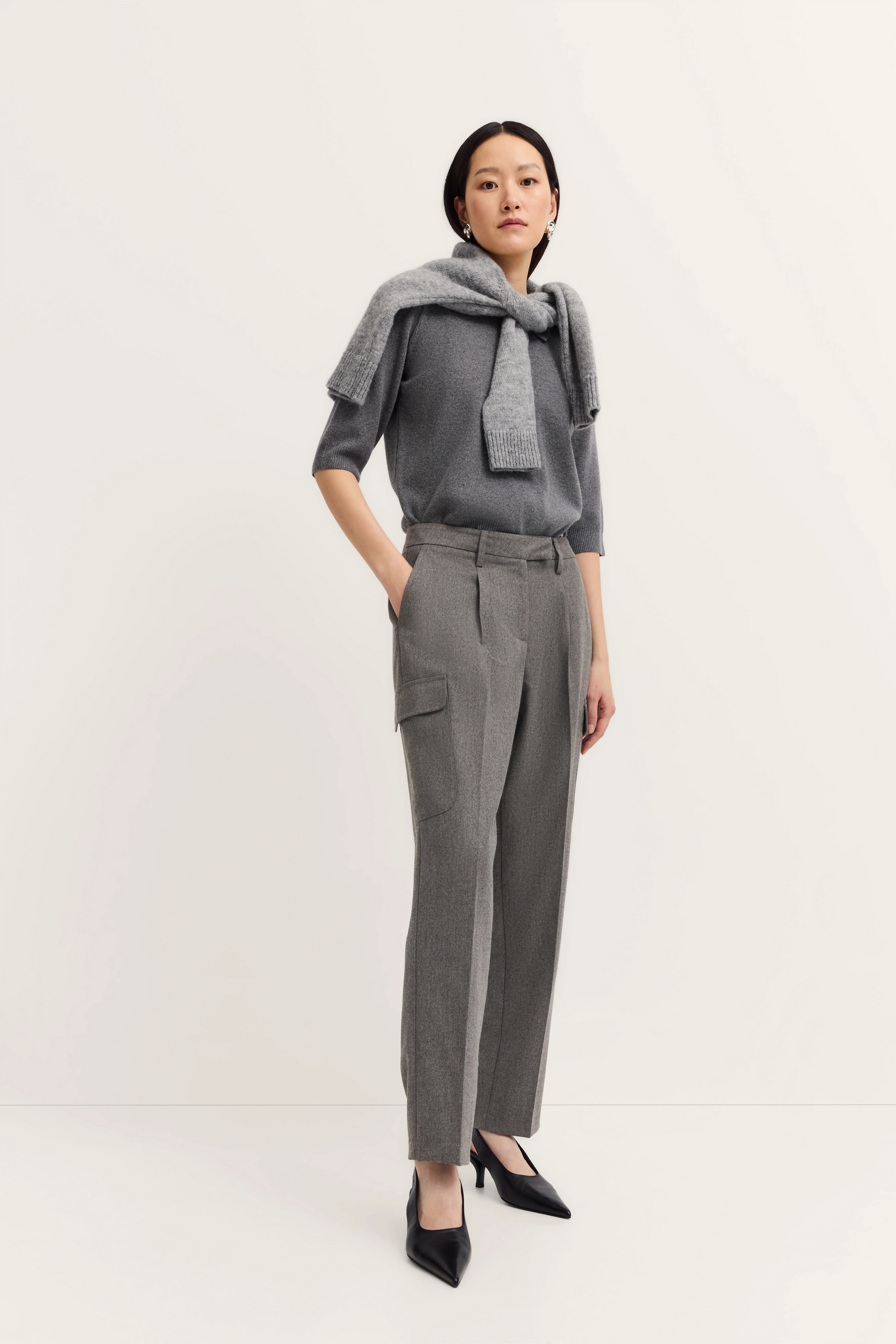 Grauer Pullover mit Schal und grauer Hose, getragen von Model, elegantes Posing.