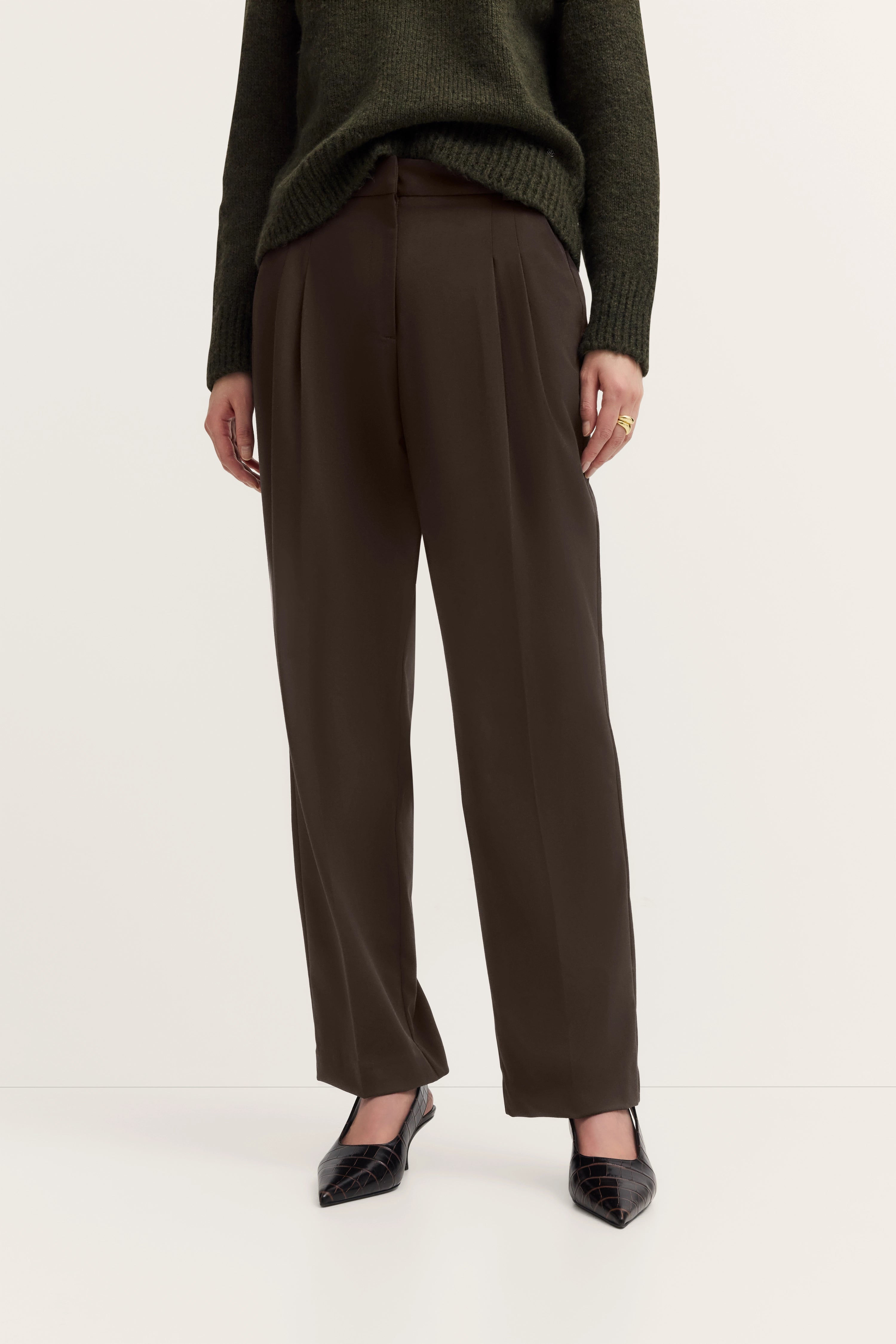 Dunkelgrüner Pullover und braune Hose, legeres Modelbild, entspannte Pose.