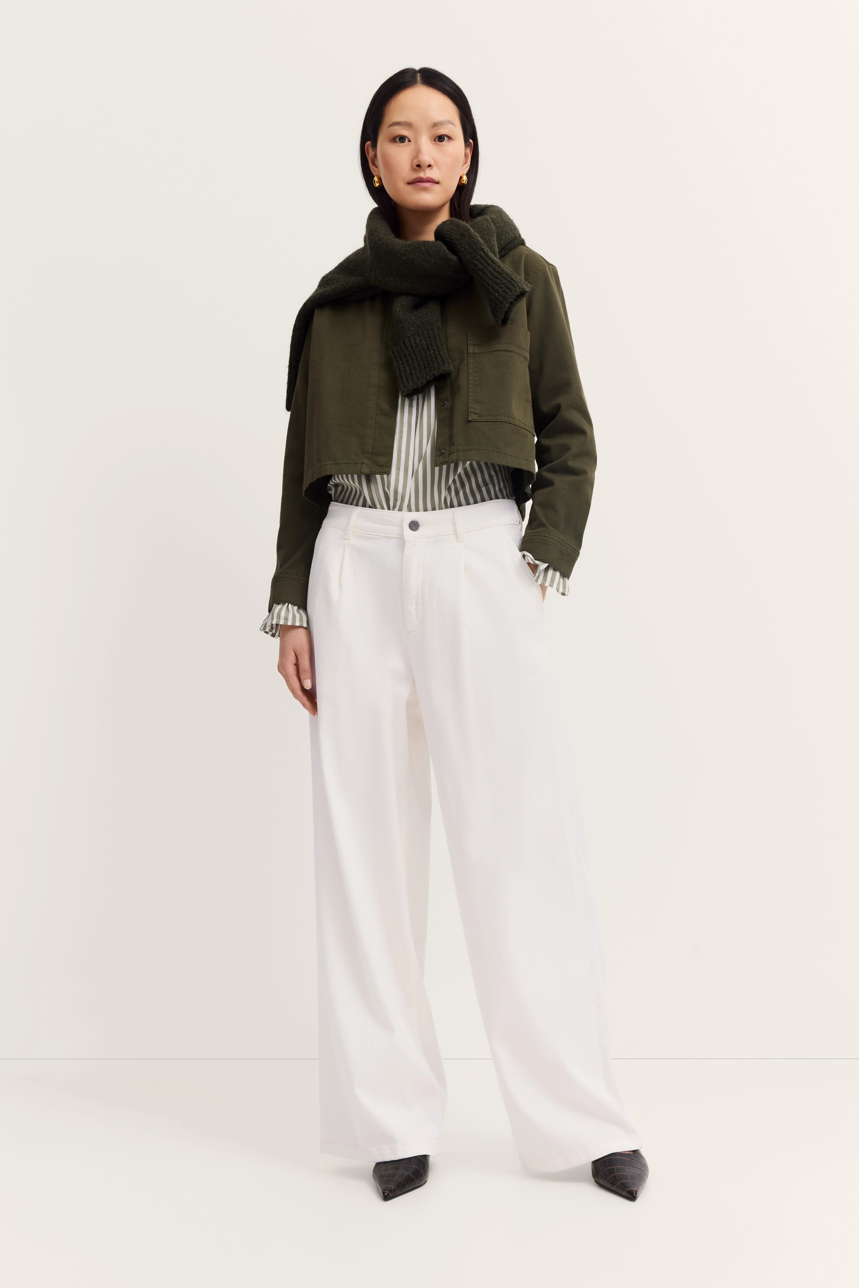 Model in olivgrüner Jacke, gestreifter Bluse, weißer Hose. Lässig stehend. Eleganz von bugatti.