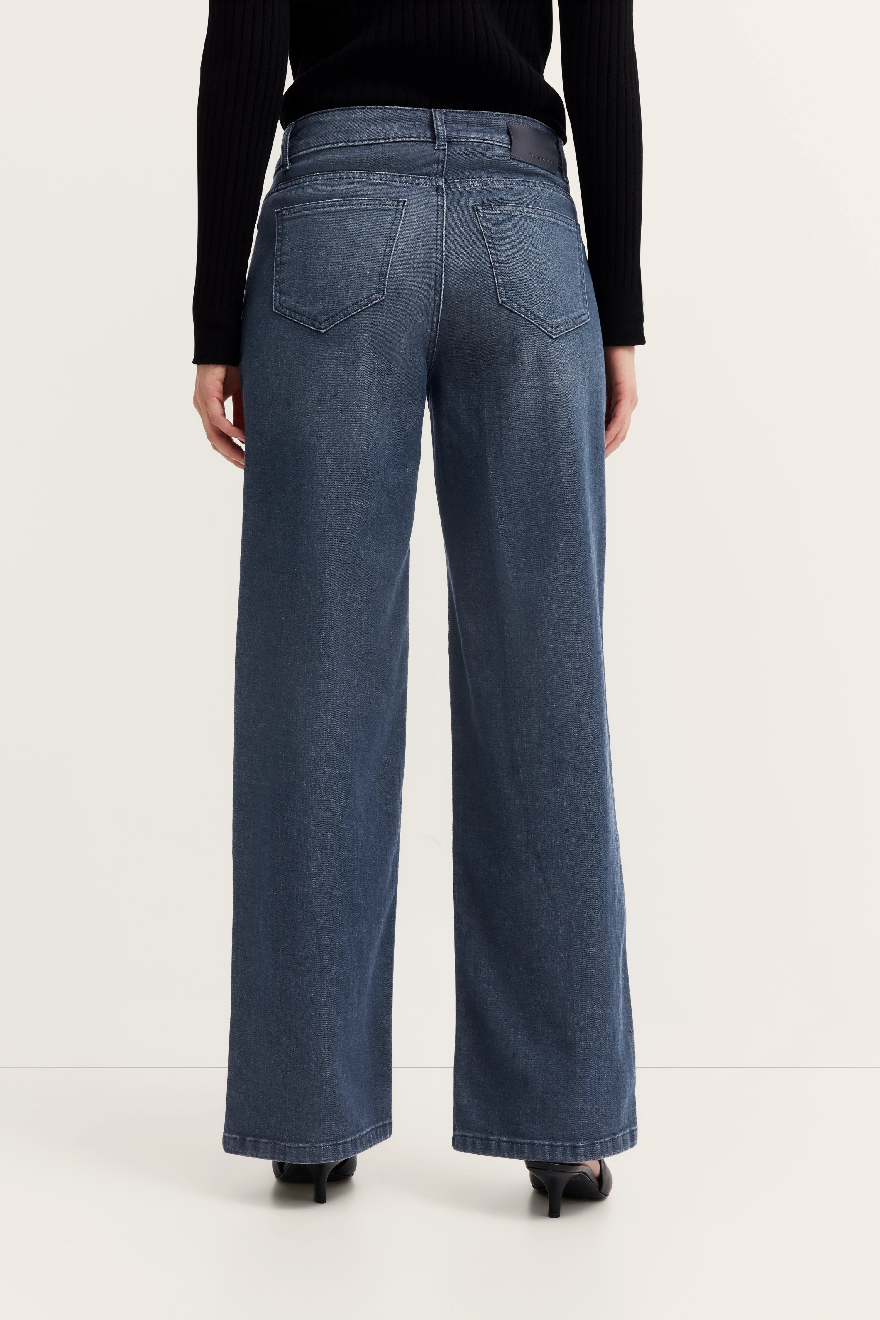 Rückansicht Modell mit blauer Jeans und schwarzem Oberteil.