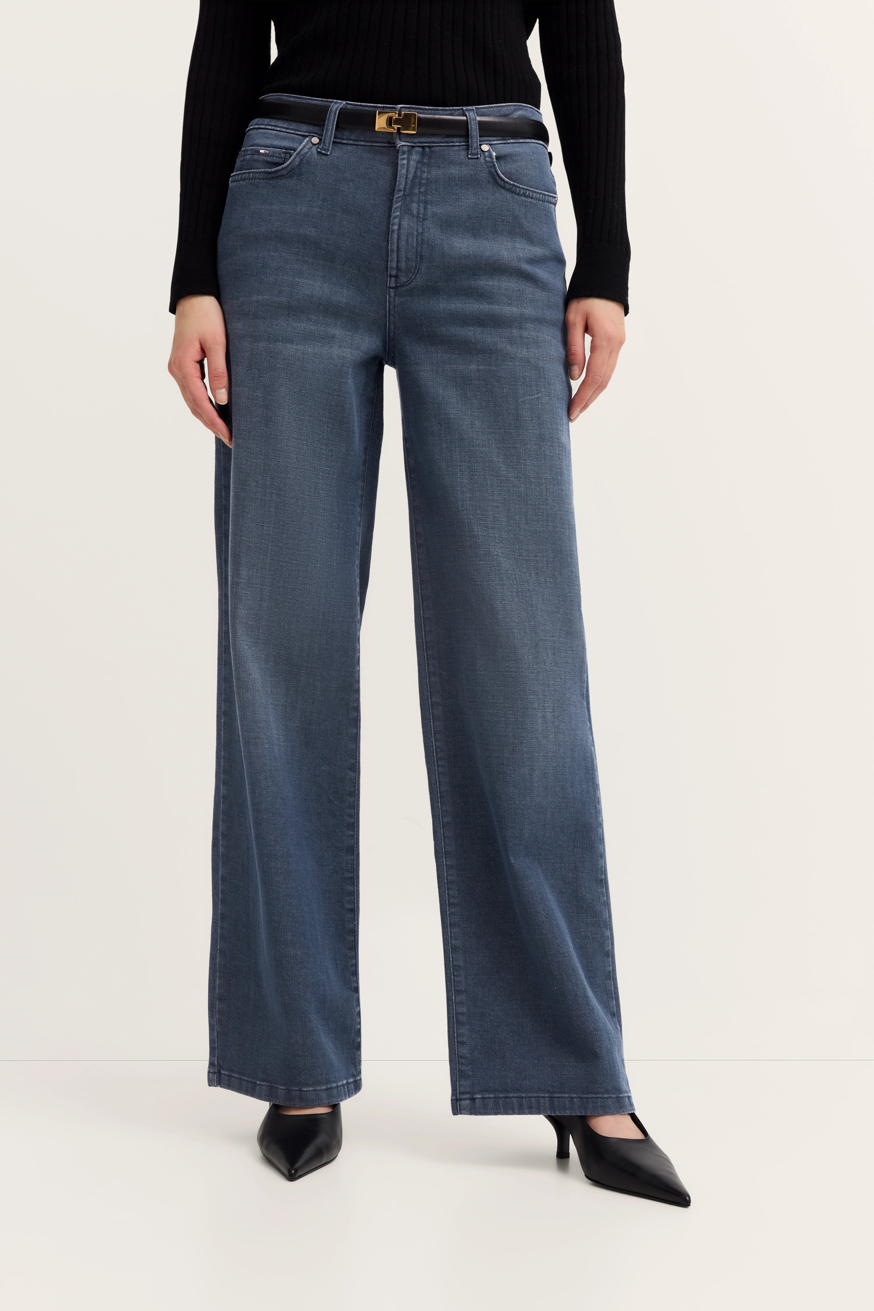 Weites Jeansoutfit in Blau mit schwarzem Pullover, Modelbild, lässiger Stand in schwarzen Pumps.