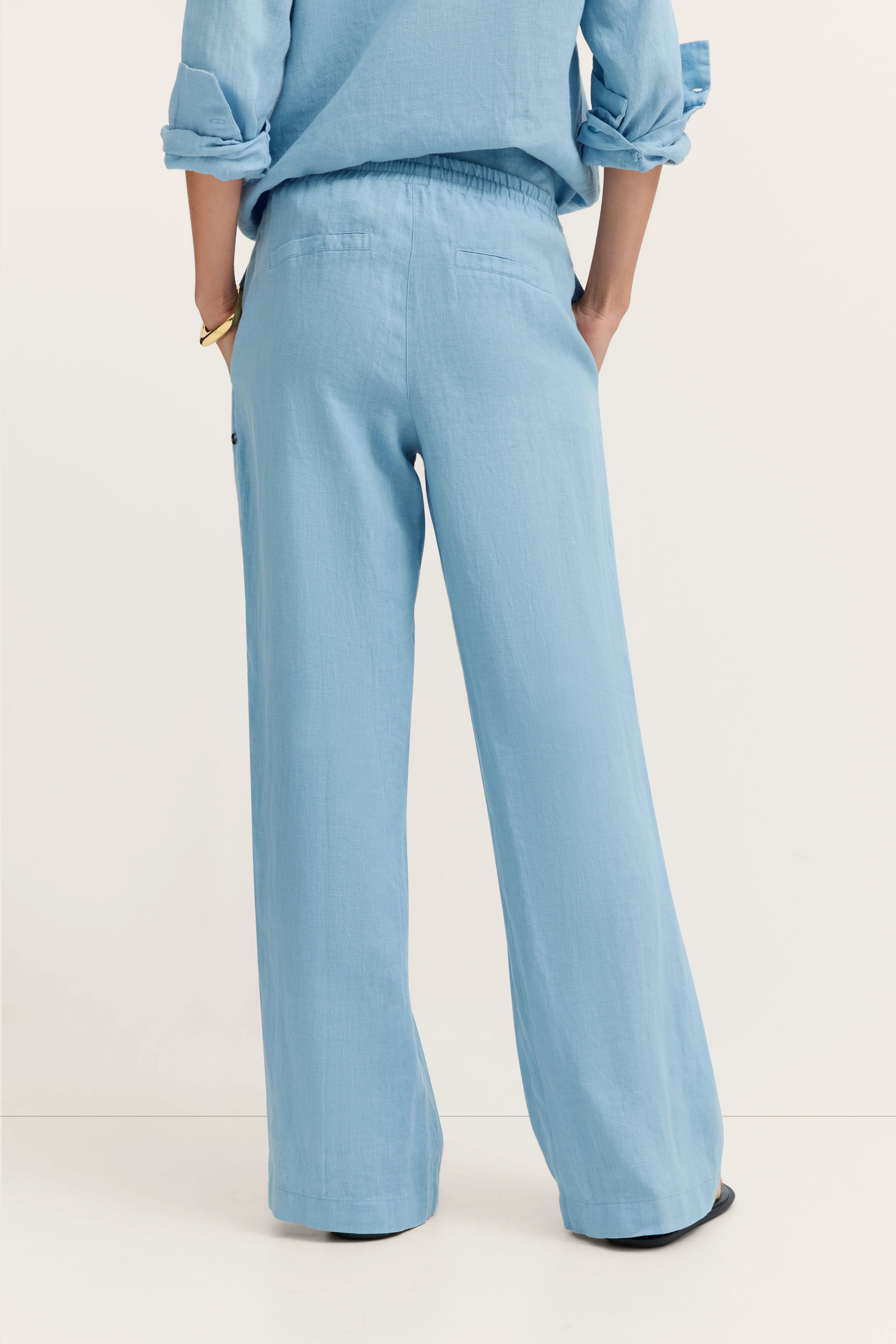 Weit geschnittene, hellblaue Leinenhose, legeres Modelbild von hinten, Hände in den Taschen.