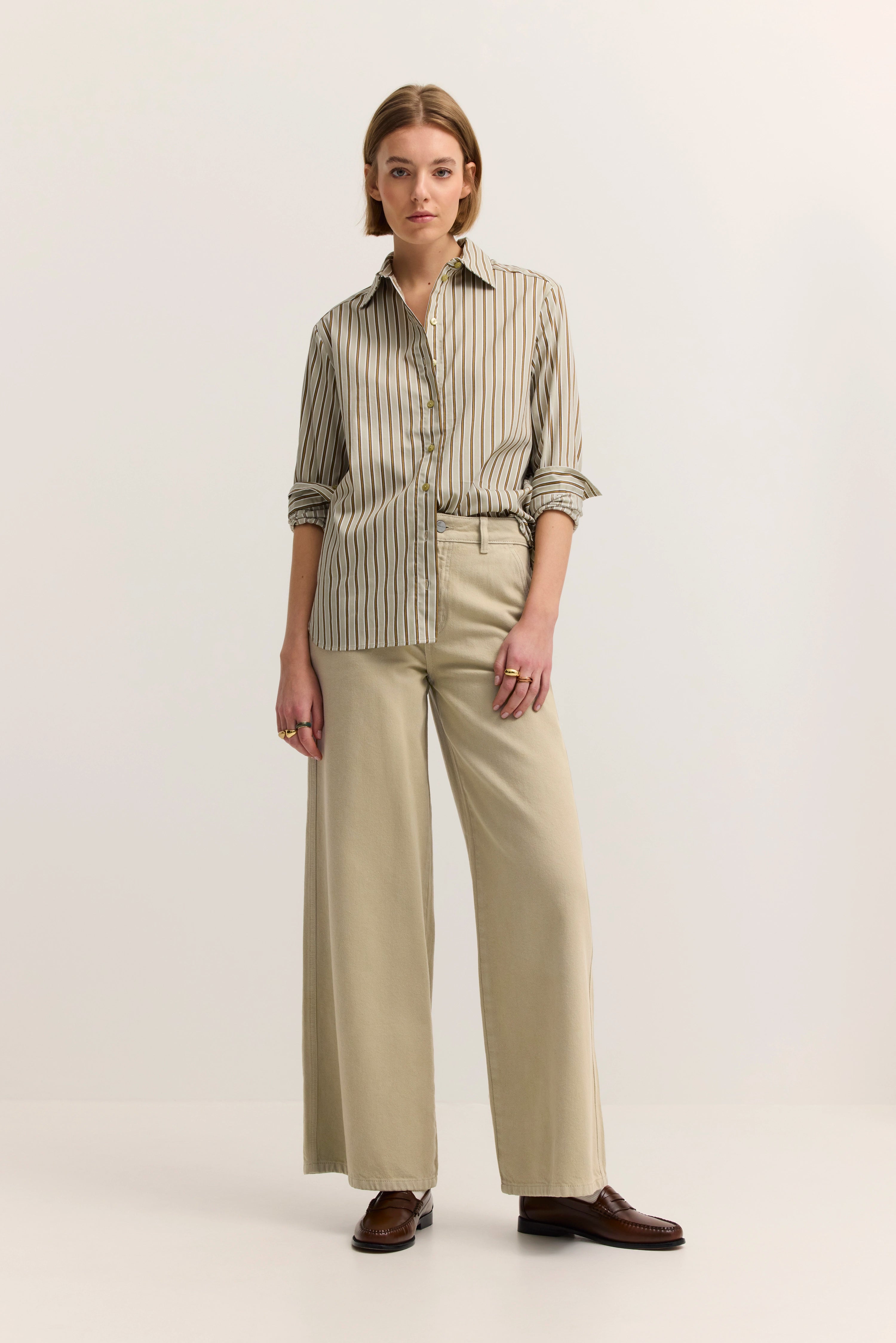 Model in gestreiftem Hemd und beigefarbenen Hosen, steht entspannt, bugatti Stil.