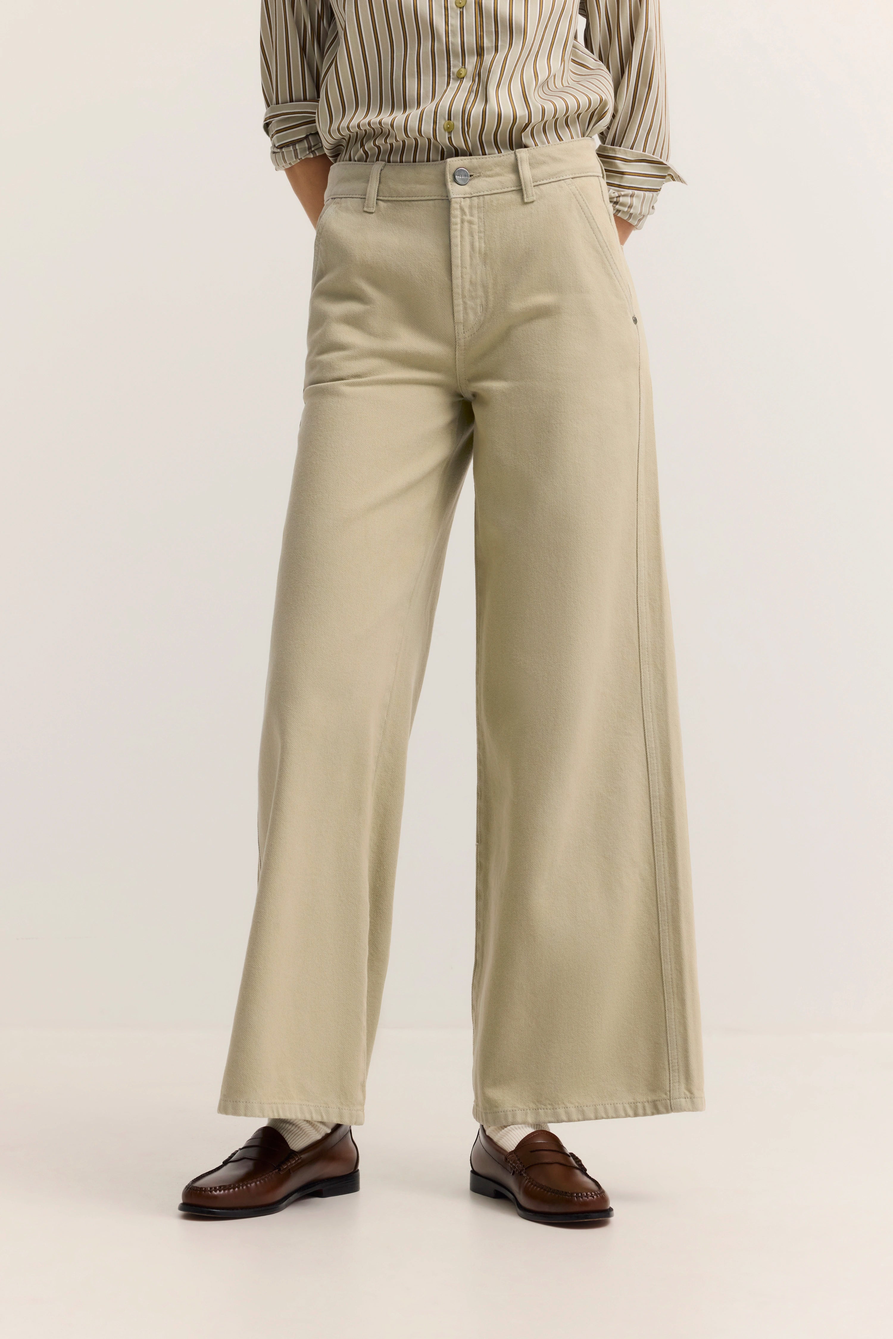 Beige weite Hose und braune Loafer, kombiniert mit gestreiftem Hemd. Büstenbild ohne Modelpose.
