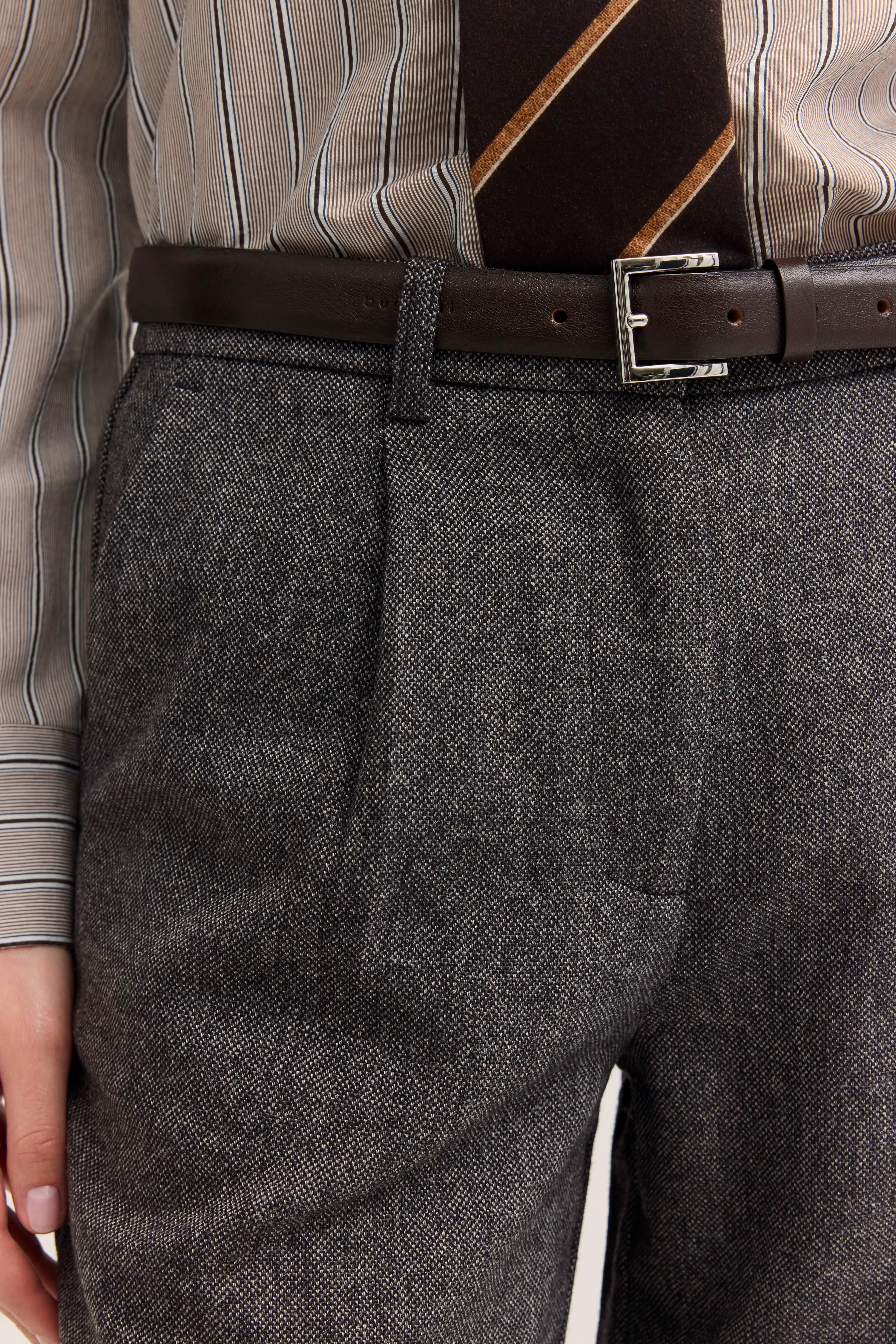 Hose in Grau mit Fischgrätmuster, gestreiftes Hemd, brauner Gürtel, Detailaufnahme.