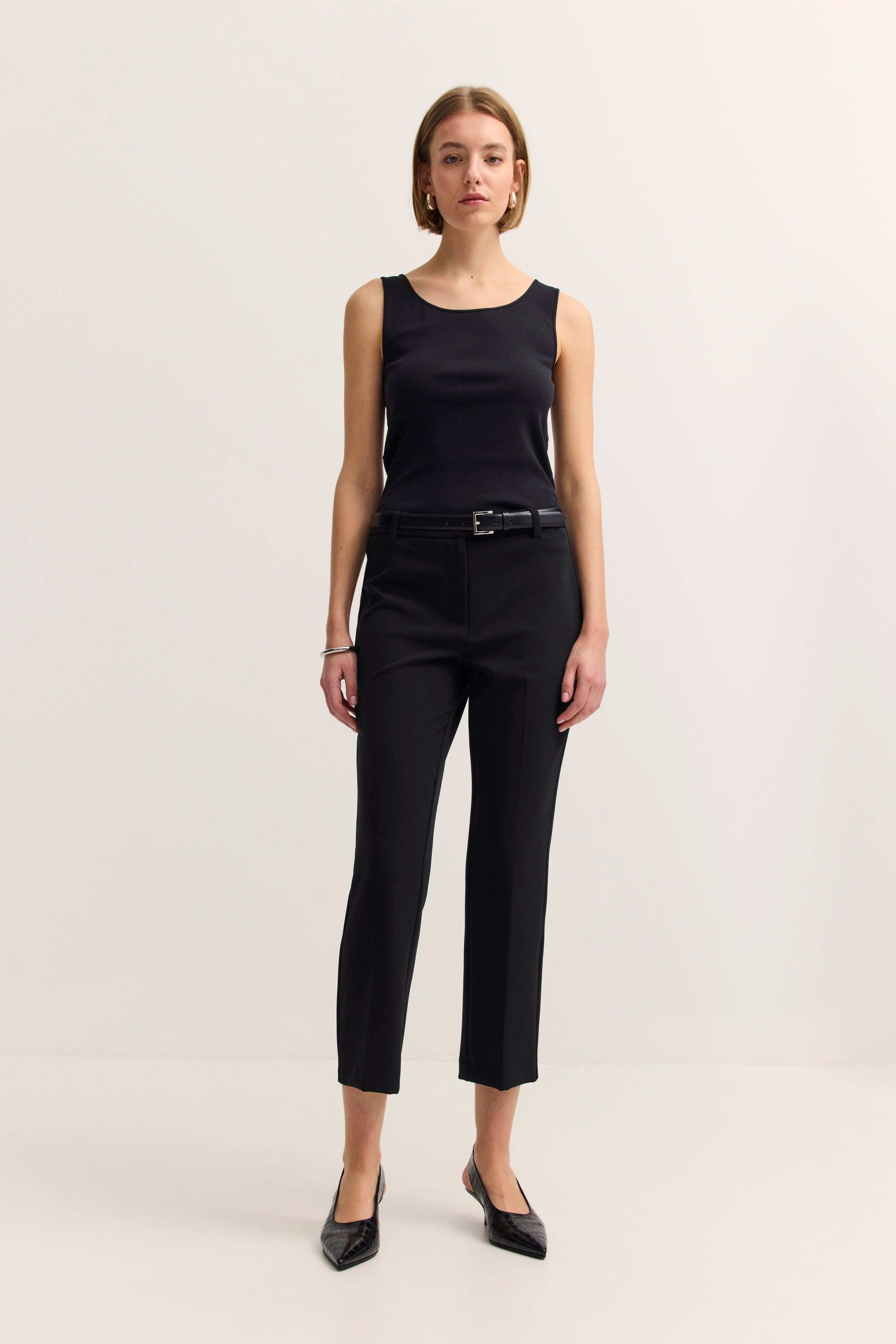 Schwarzes ärmelloses Top und Hose, Model posiert stehend, eleganter Look von bugatti.