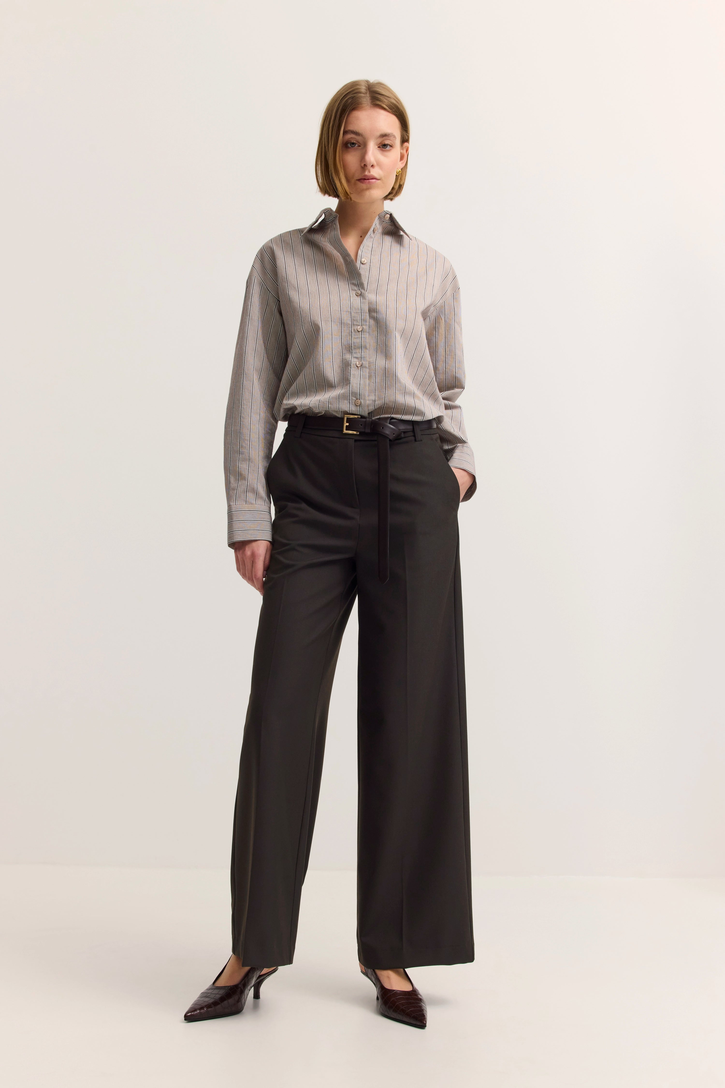 Model in gestreifter Bluse und schwarzen Hosen, entspanntes Standing-Pose, bugatti Stil.