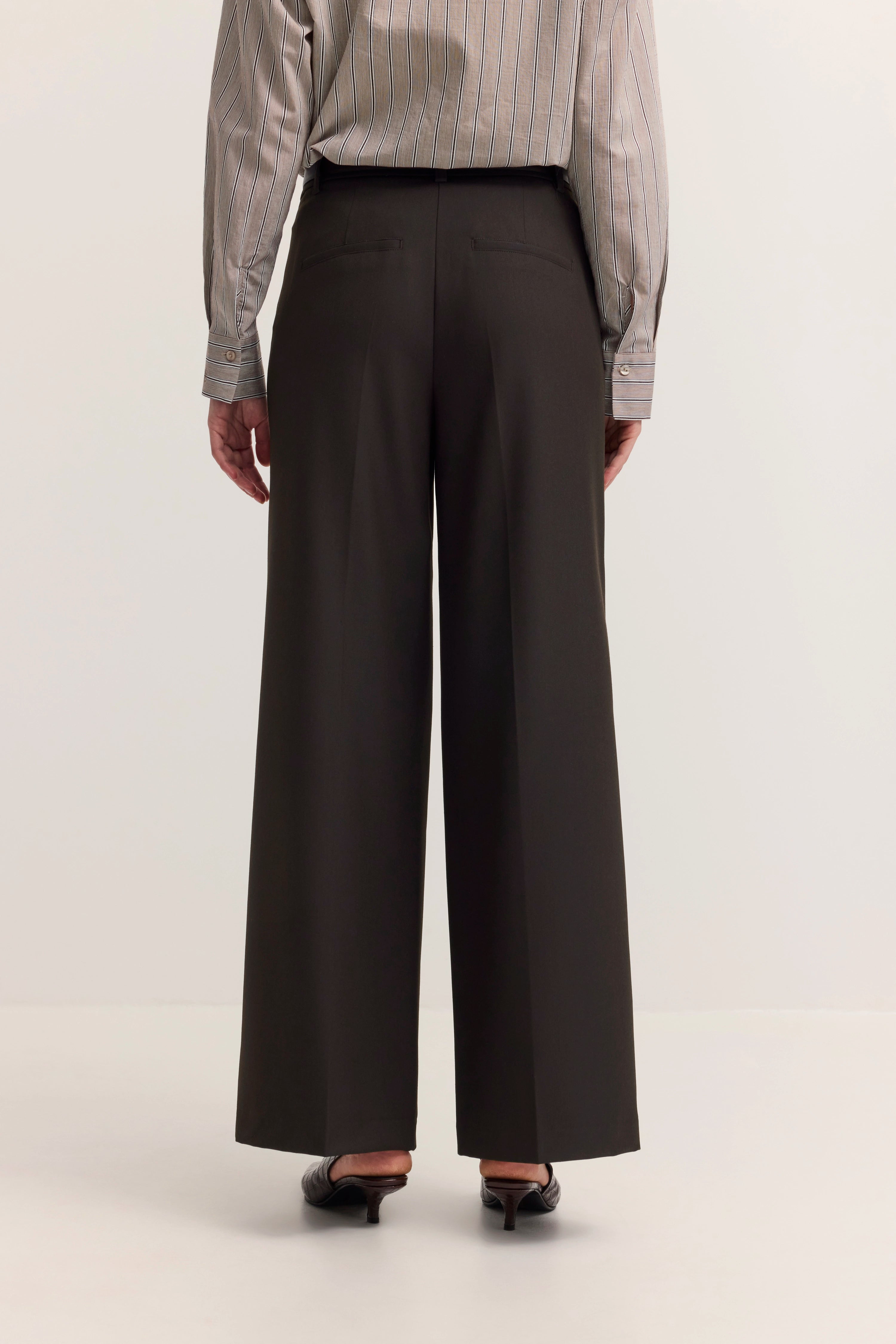 Rückansicht: Streifenbluse beige-schwarz, weite schwarze Hose, legeres Modelbild in eleganter Pose.