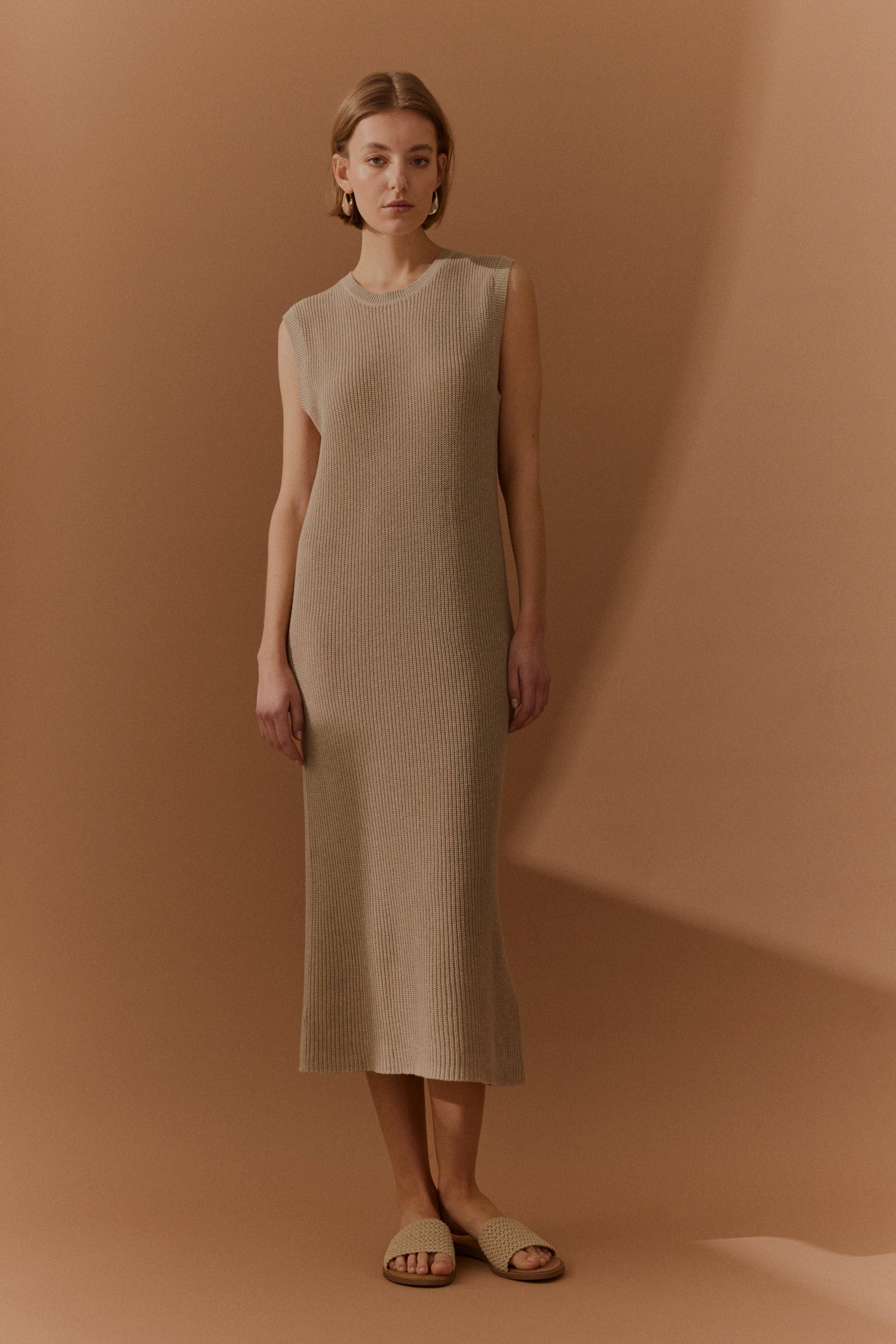Ärmelloses, beigefarbenes Strickkleid, Model posiert stehend, bugatti Stil und Eleganz.
