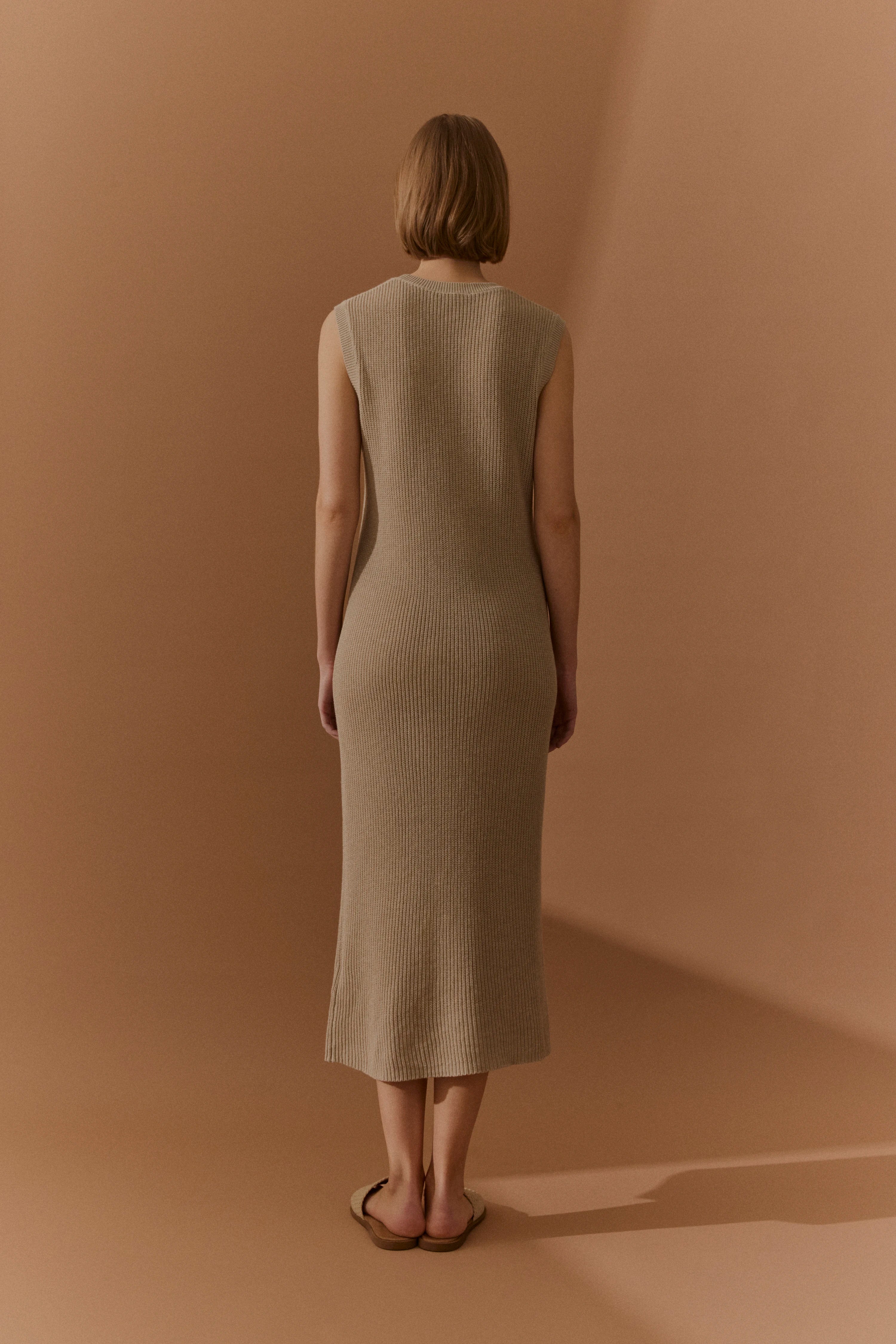 Langes, ärmelloses, beigefarbenes Strickkleid, Model von hinten, entspannte Pose.