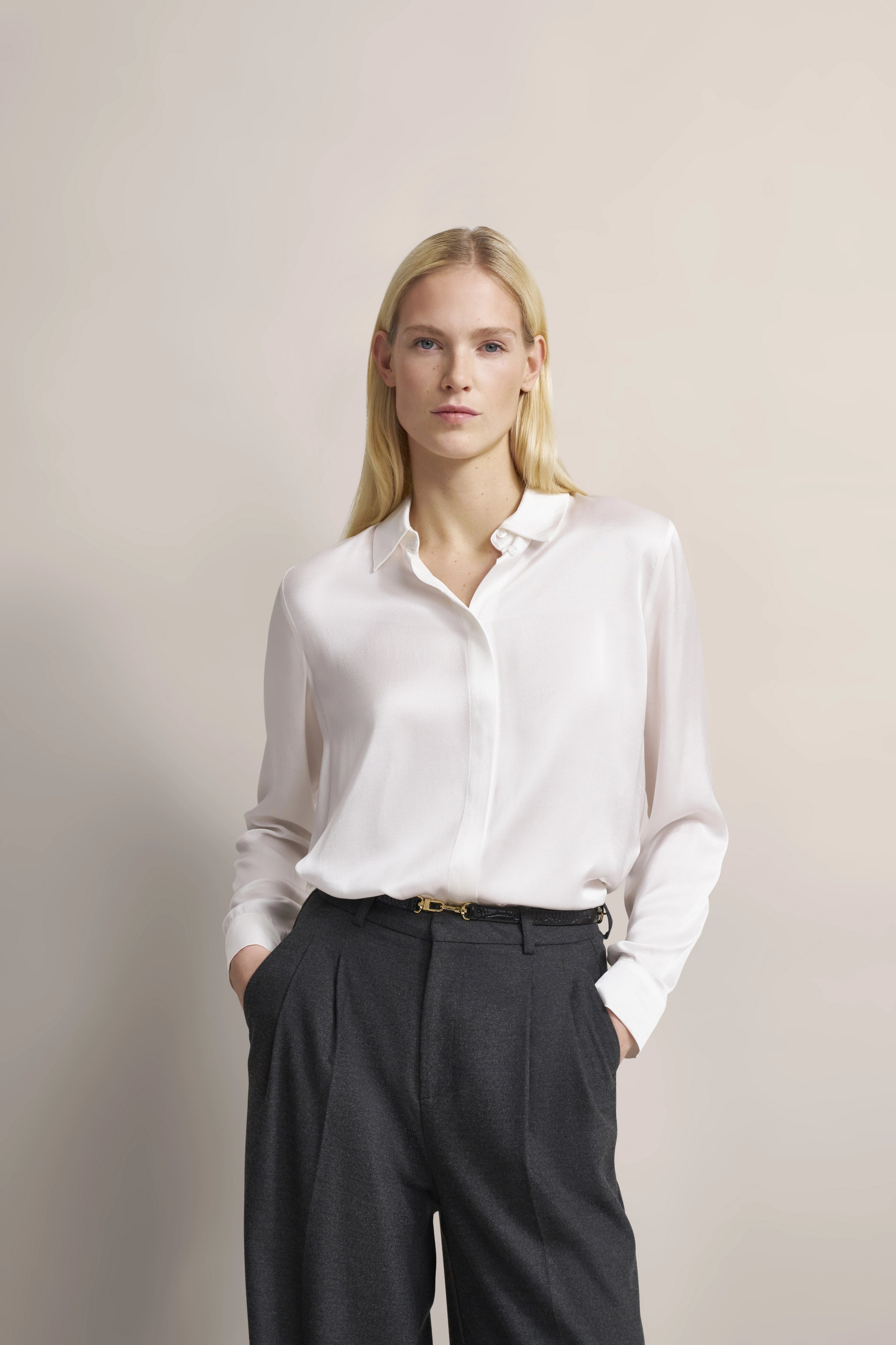 Elegantes bugatti Outfit: weiße Bluse, graue Hose, Modelbild, lässige Pose, Hände in Hosentaschen.