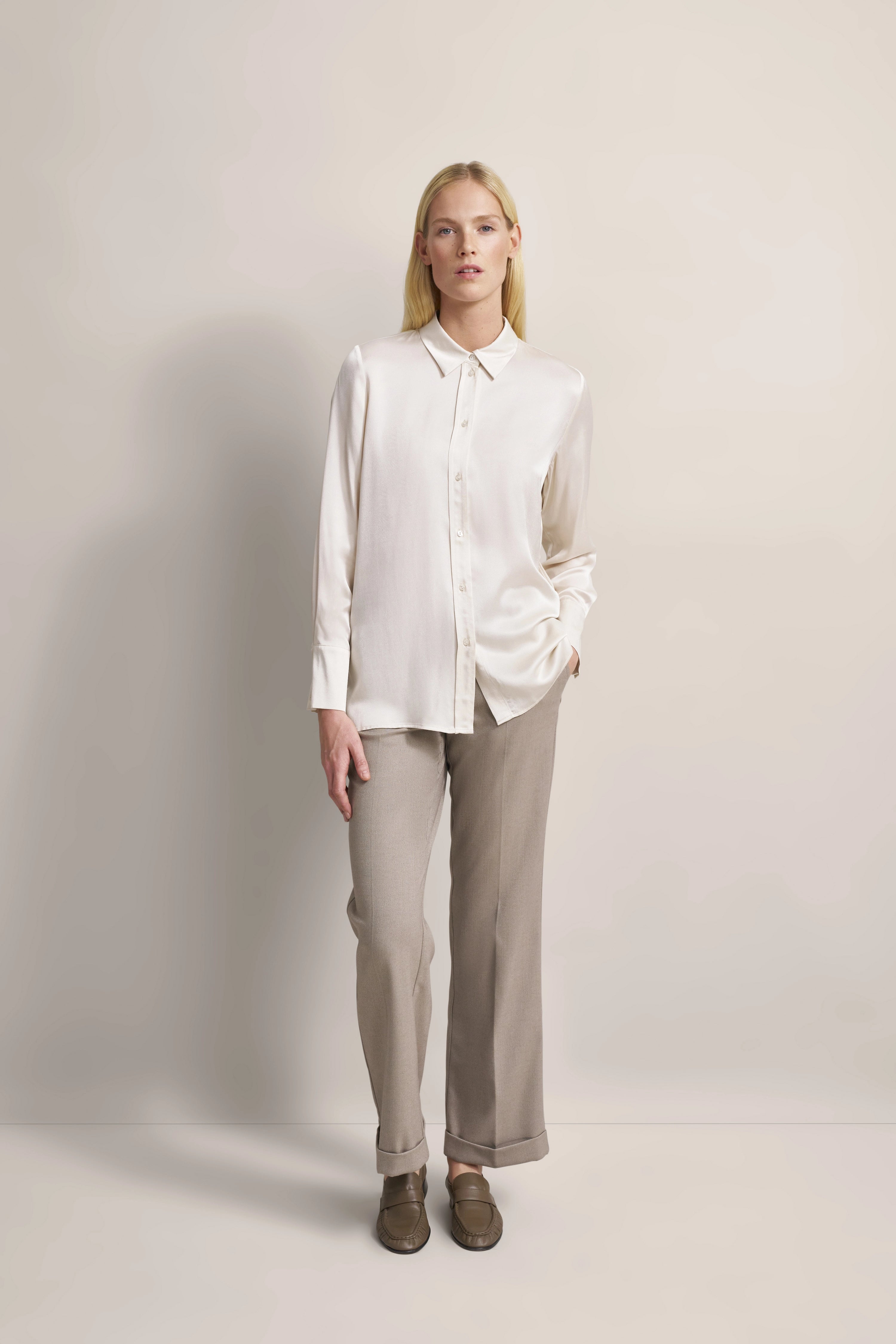 Elegantes bugatti Outfit: cremefarbene Bluse, beige Hose. Modelbild mit entspannter Pose.
