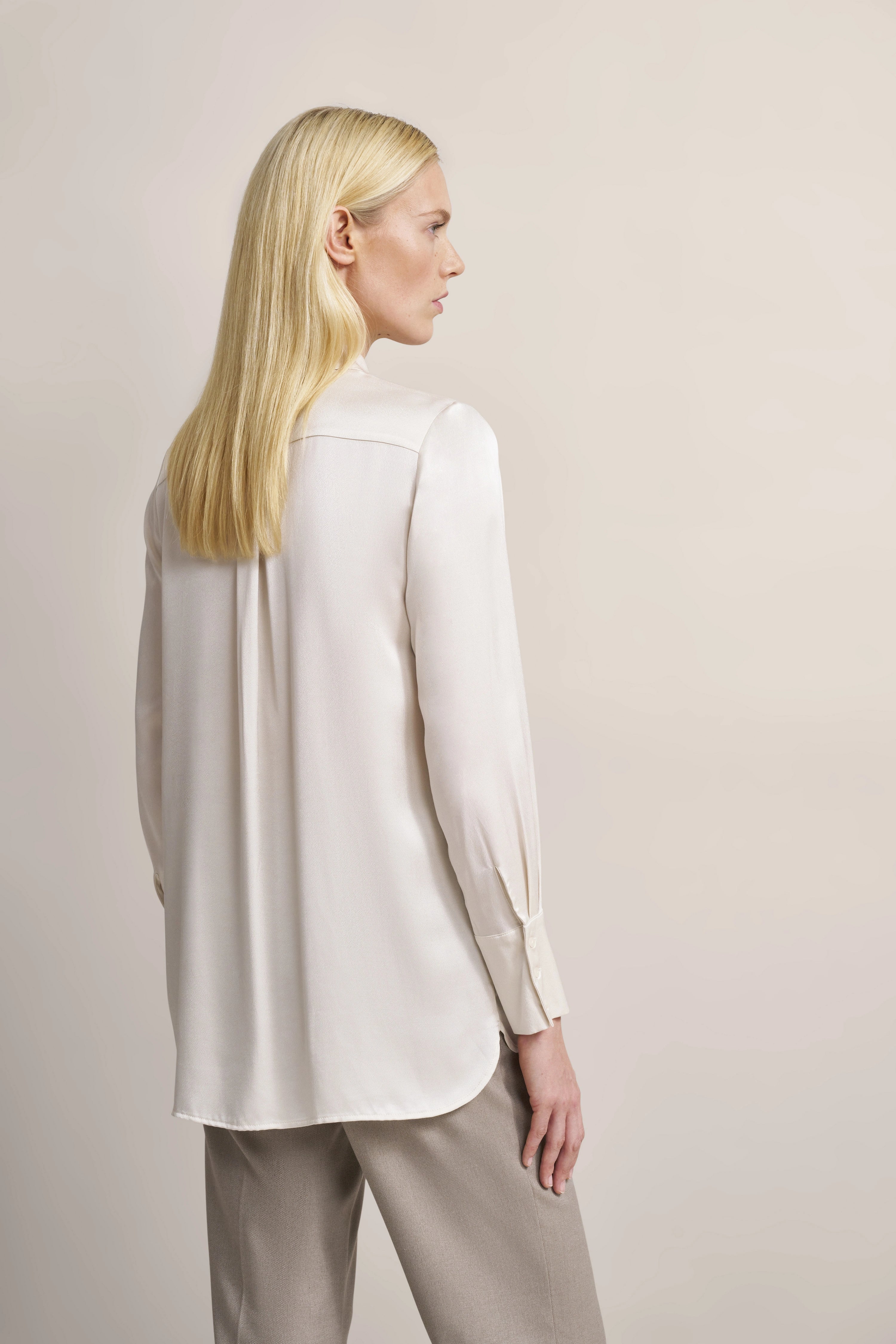 Model seitlich, trägt cremefarbene Bluse und graue Hose von bugatti, eleganter, entspannter Look.