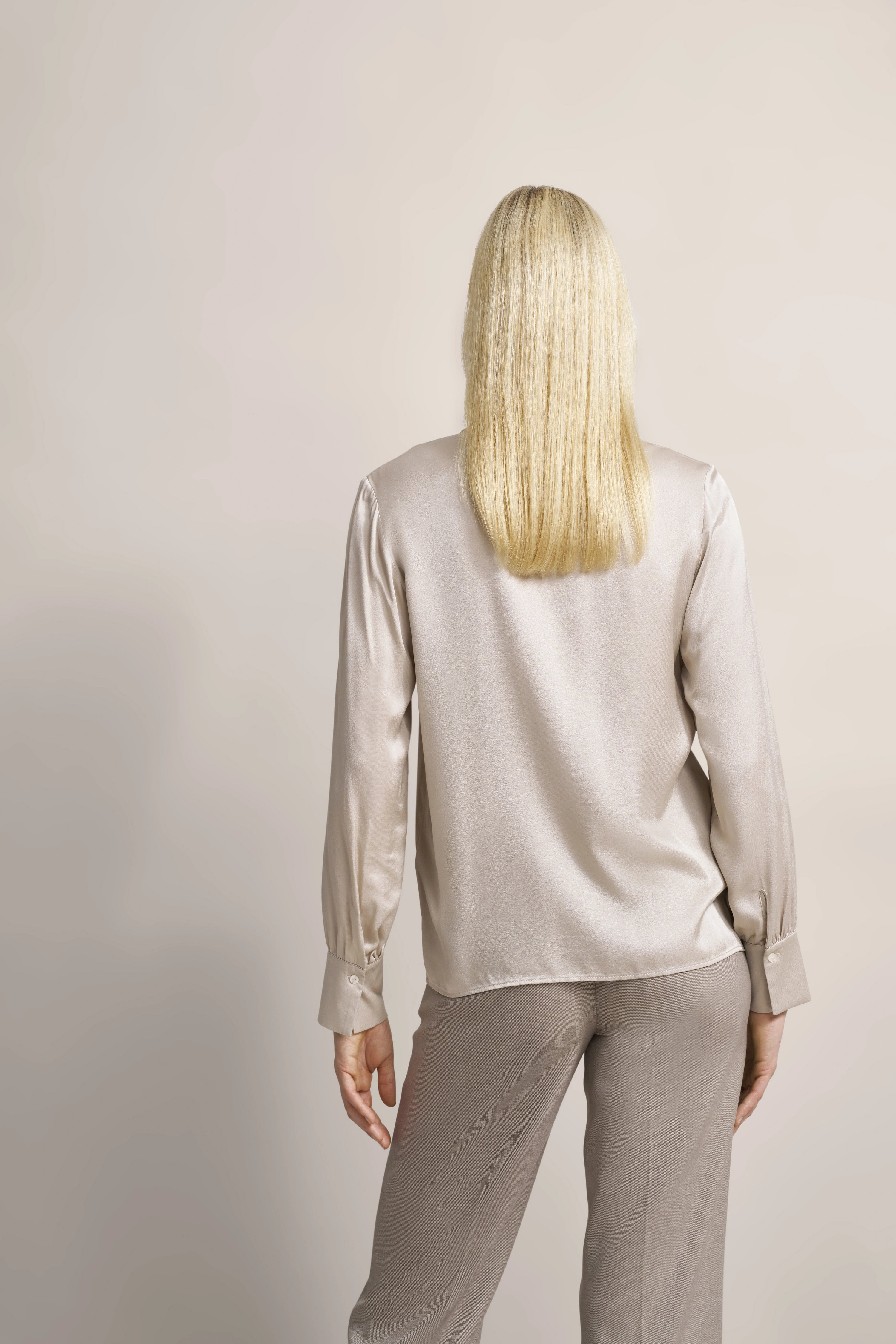 Elegantes Model in beiger Satinbluse und Hose von bugatti, Rückansicht, stehend.