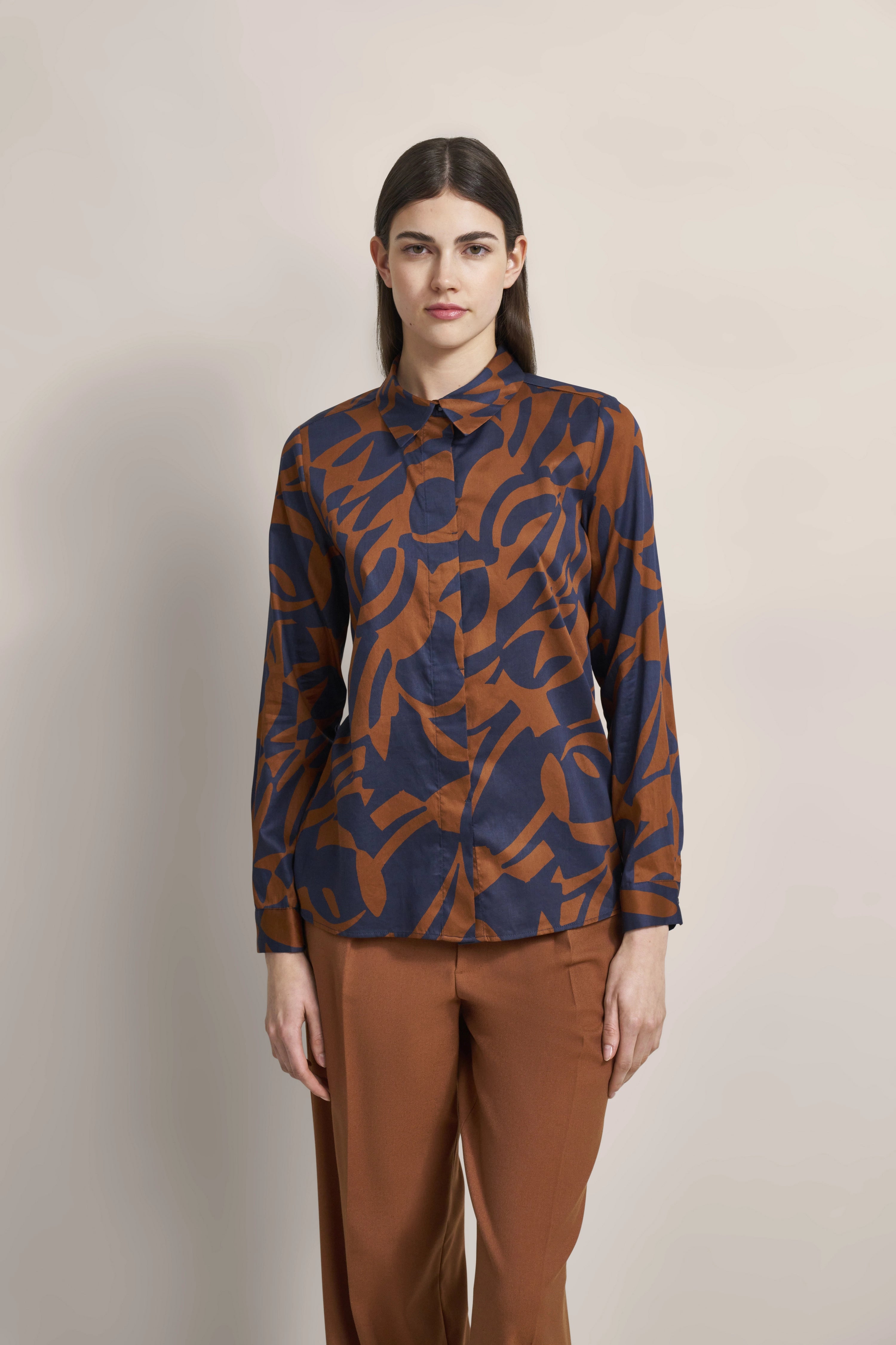 Bluse mit braun-blauem Muster, kombiniert mit brauner Hose, Modelbild, entspannte Pose.