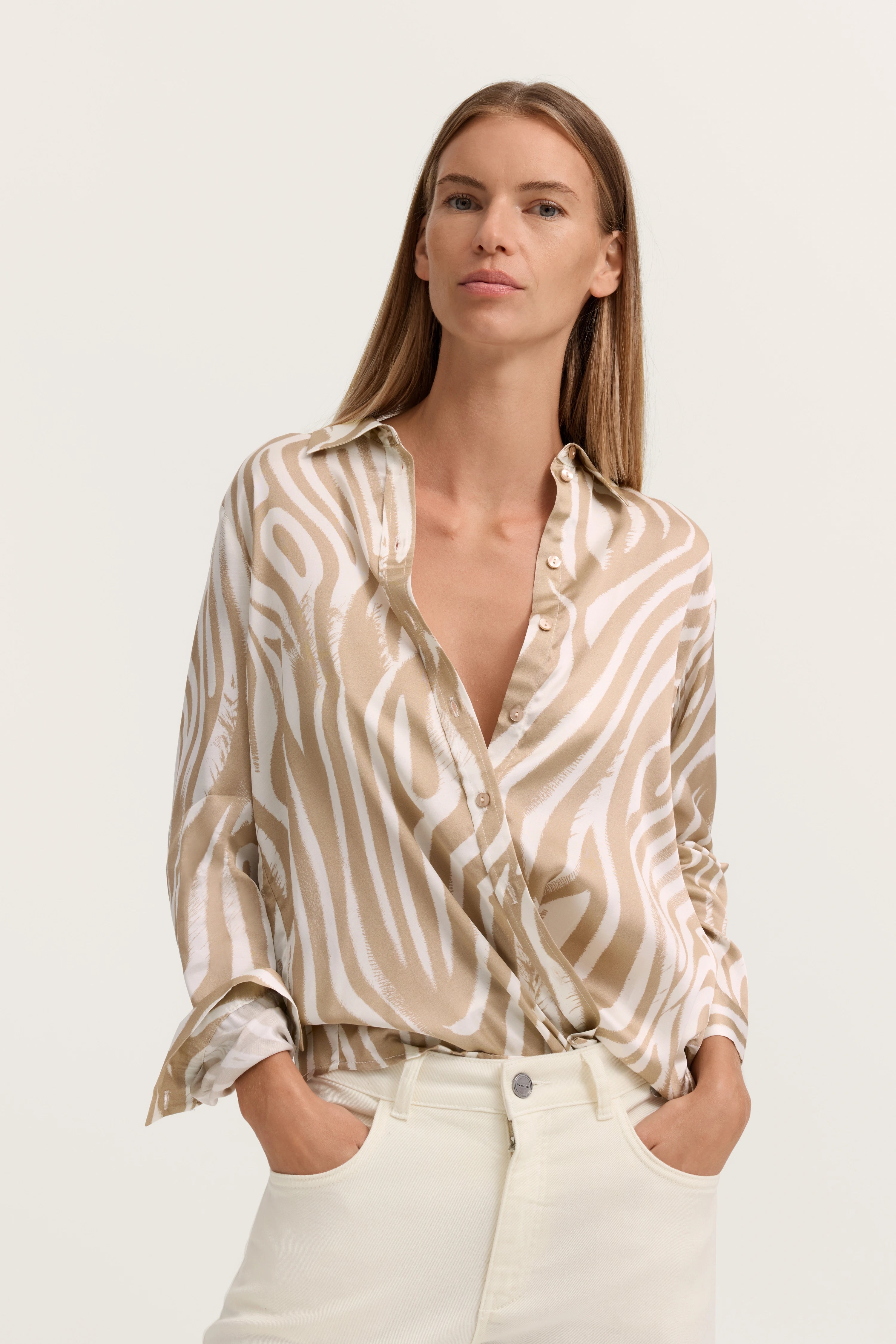 Elegante Bluse mit beige-weißem Zebradesign, getragen von Model mit Händen in Hosentaschen.
