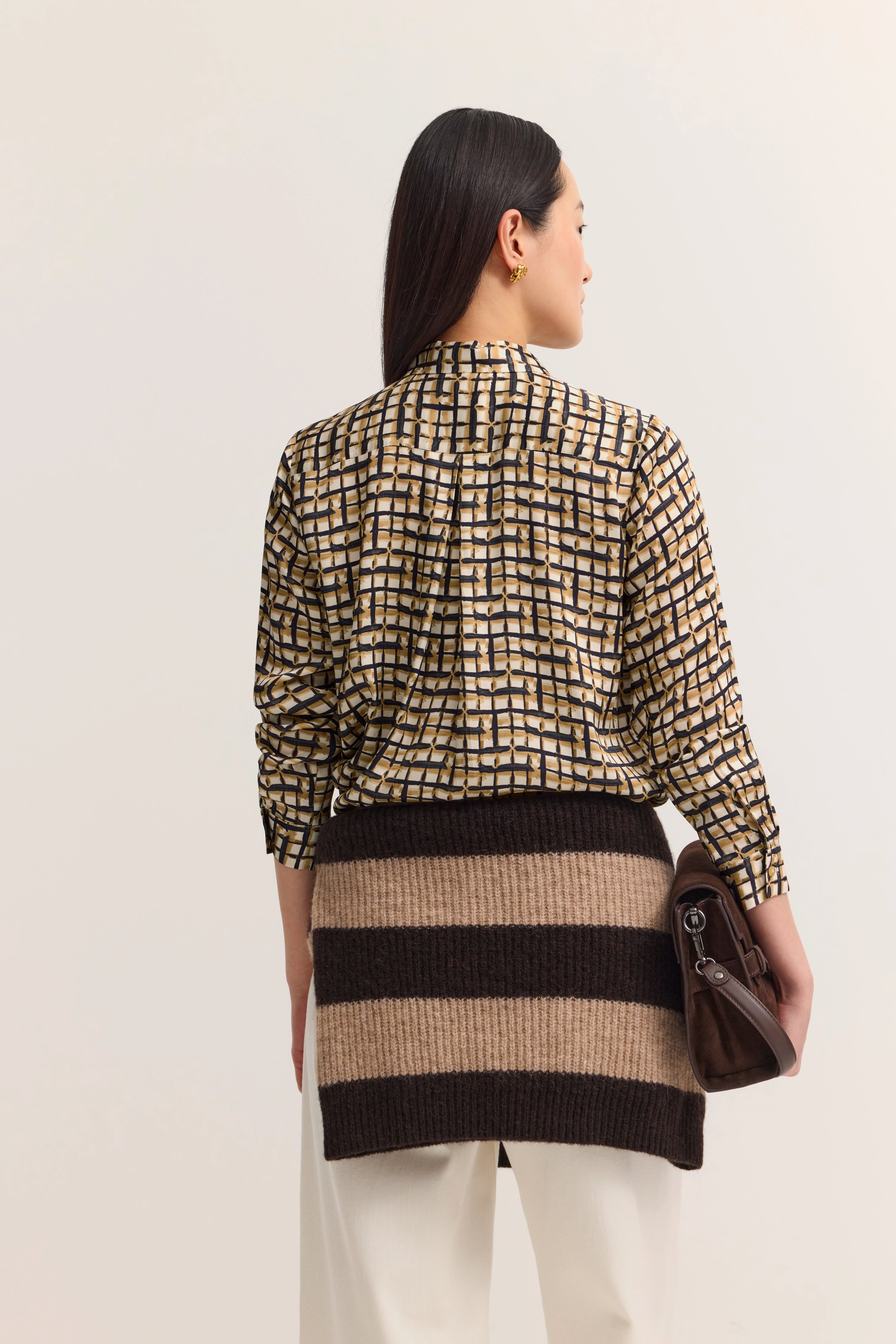 Modelbild von hinten, gemusterte bugatti Bluse in Beige-Schwarz mit gestreiftem Rock, lässig posierend.