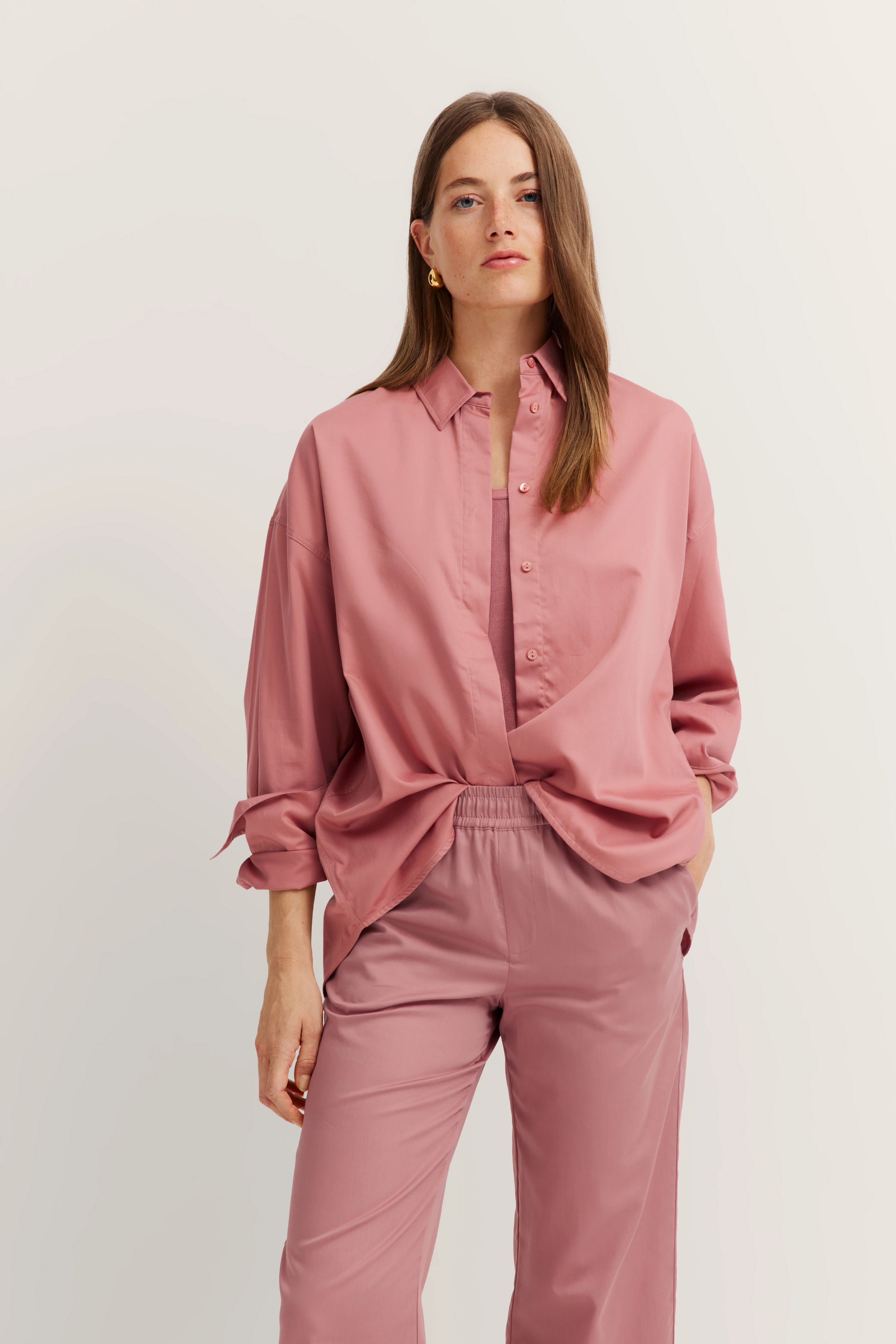 Model in rosa bugatti Bluse und Hose, legeres Posing mit einer Hand in der Tasche.