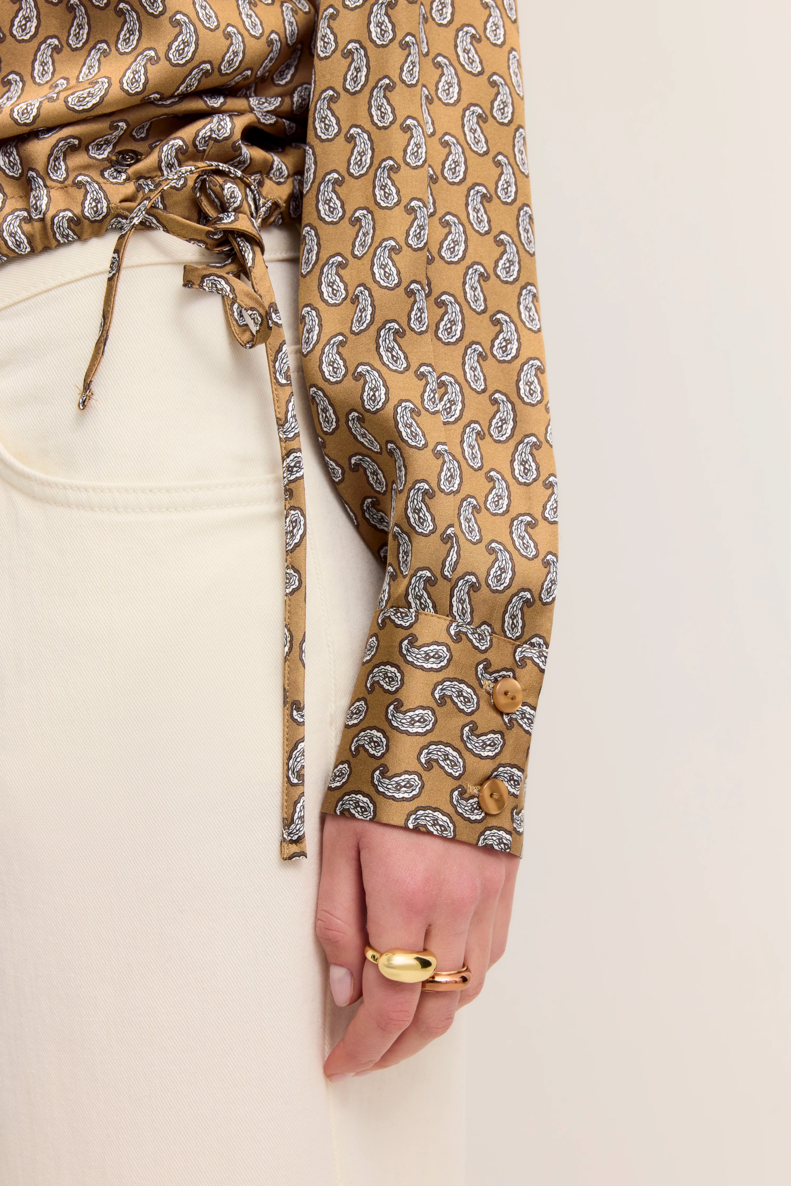 Beige gemusterte Paisley-Bluse mit Knoten, kombiniert mit cremefarbener Hose, Detailaufnahme.