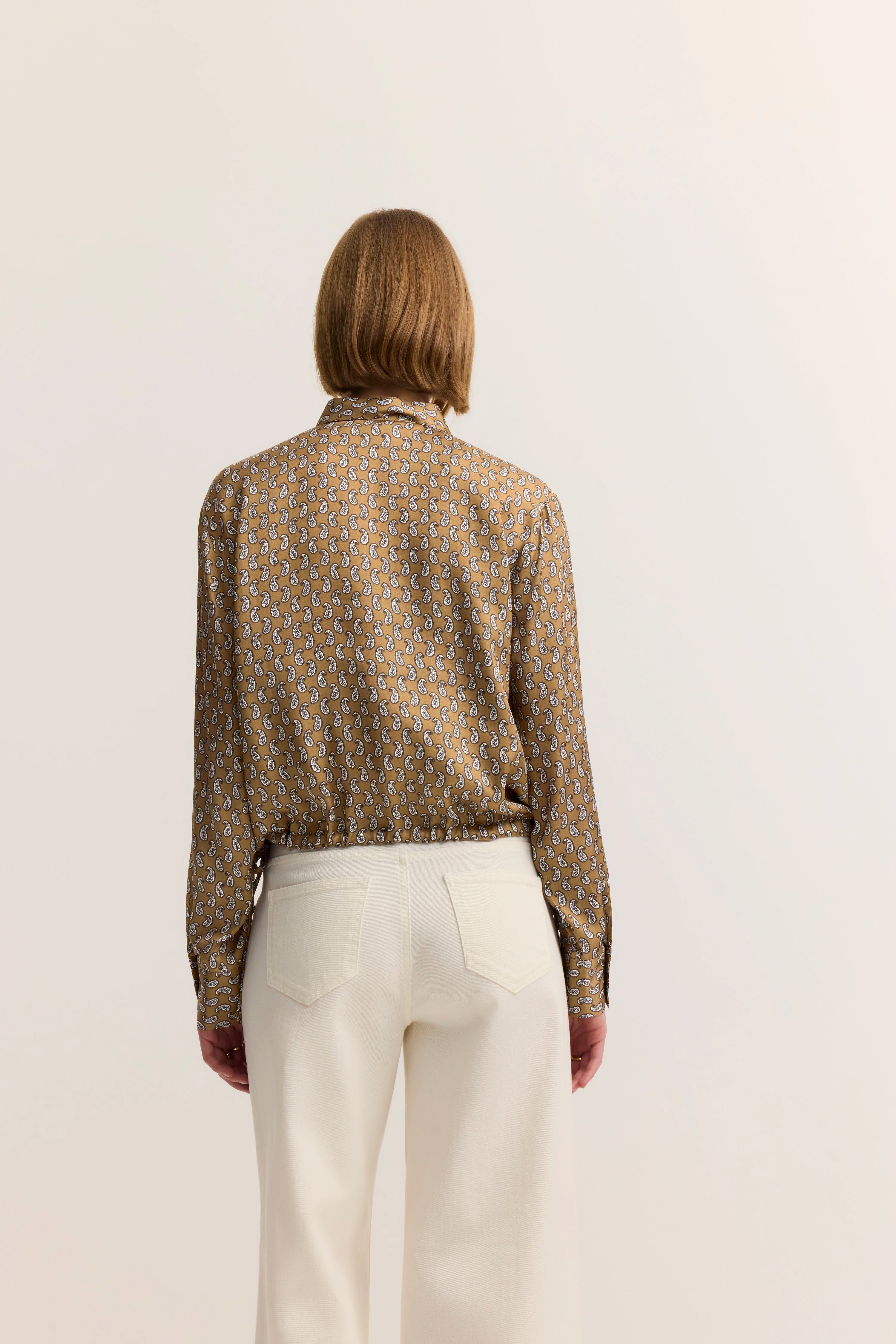 Bluse mit Paisleymuster in Braun, weiße Hose, Modelbild von hinten, entspannte Pose.