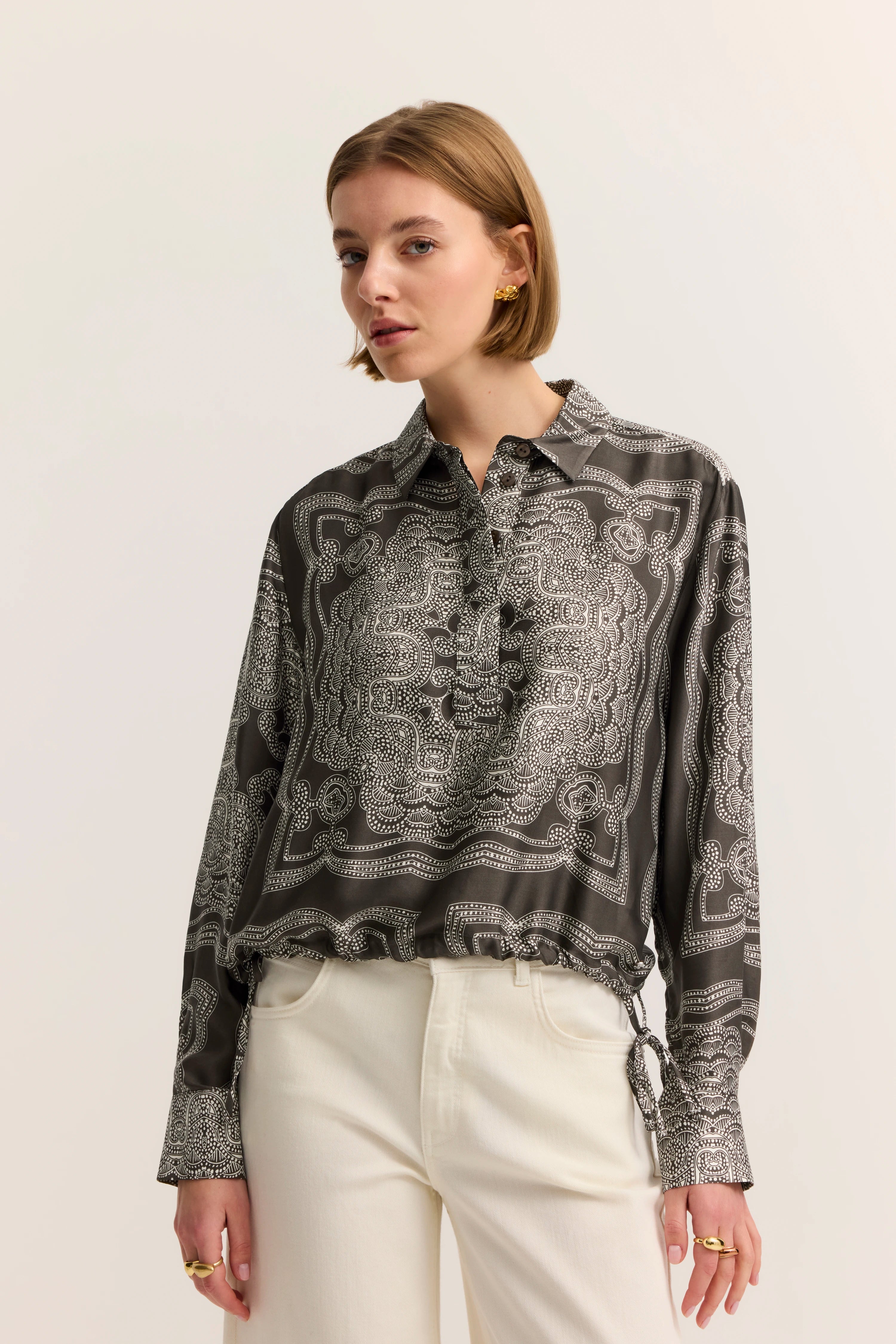 Bluse mit schwarz-weißem Muster, Modelbild, lässige Pose, kombiniert mit cremefarbenen Hosen.