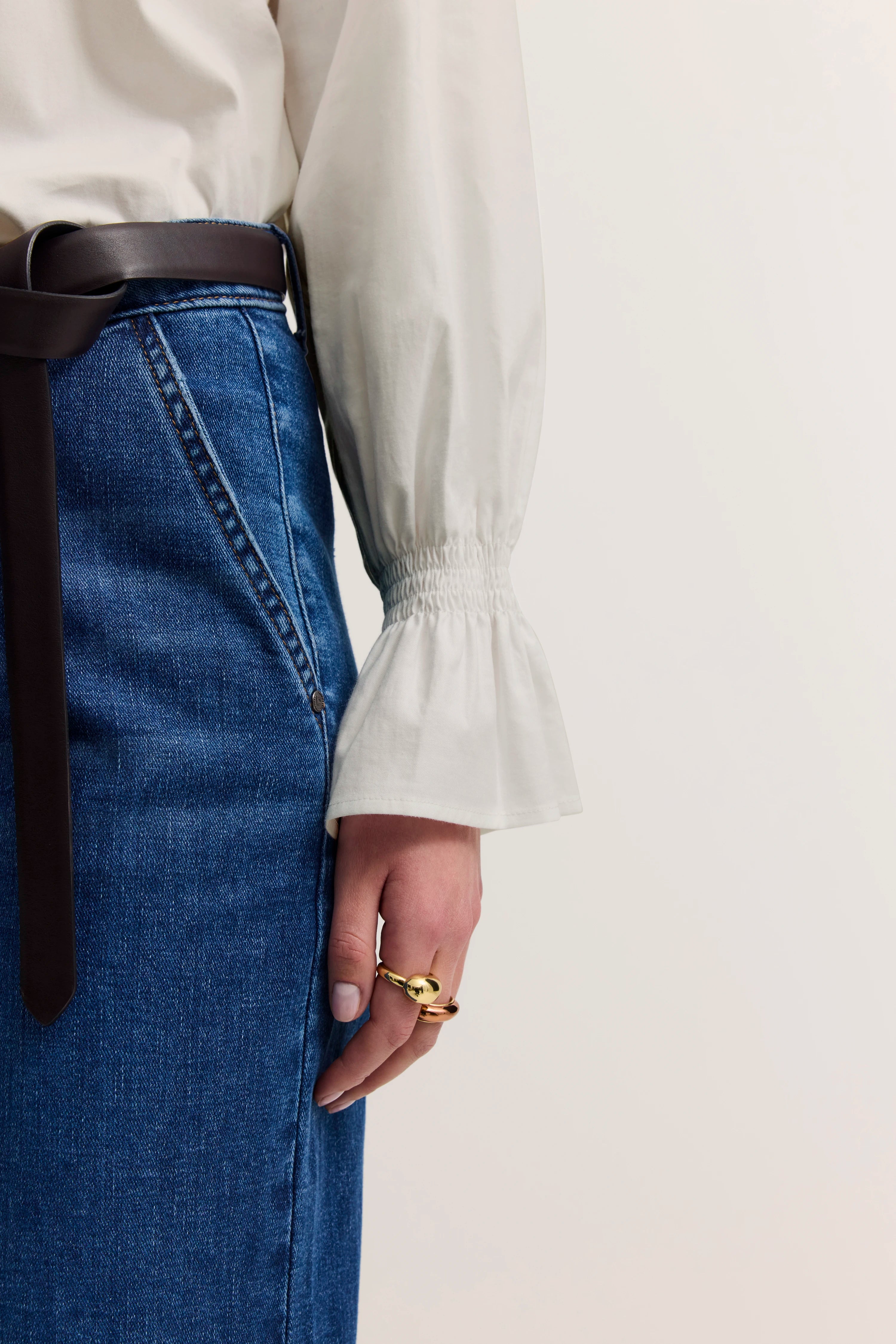 Weiße Bluse mit Glockenärmeln und blauer Jeans, Detailansicht mit braunem Gürtel.