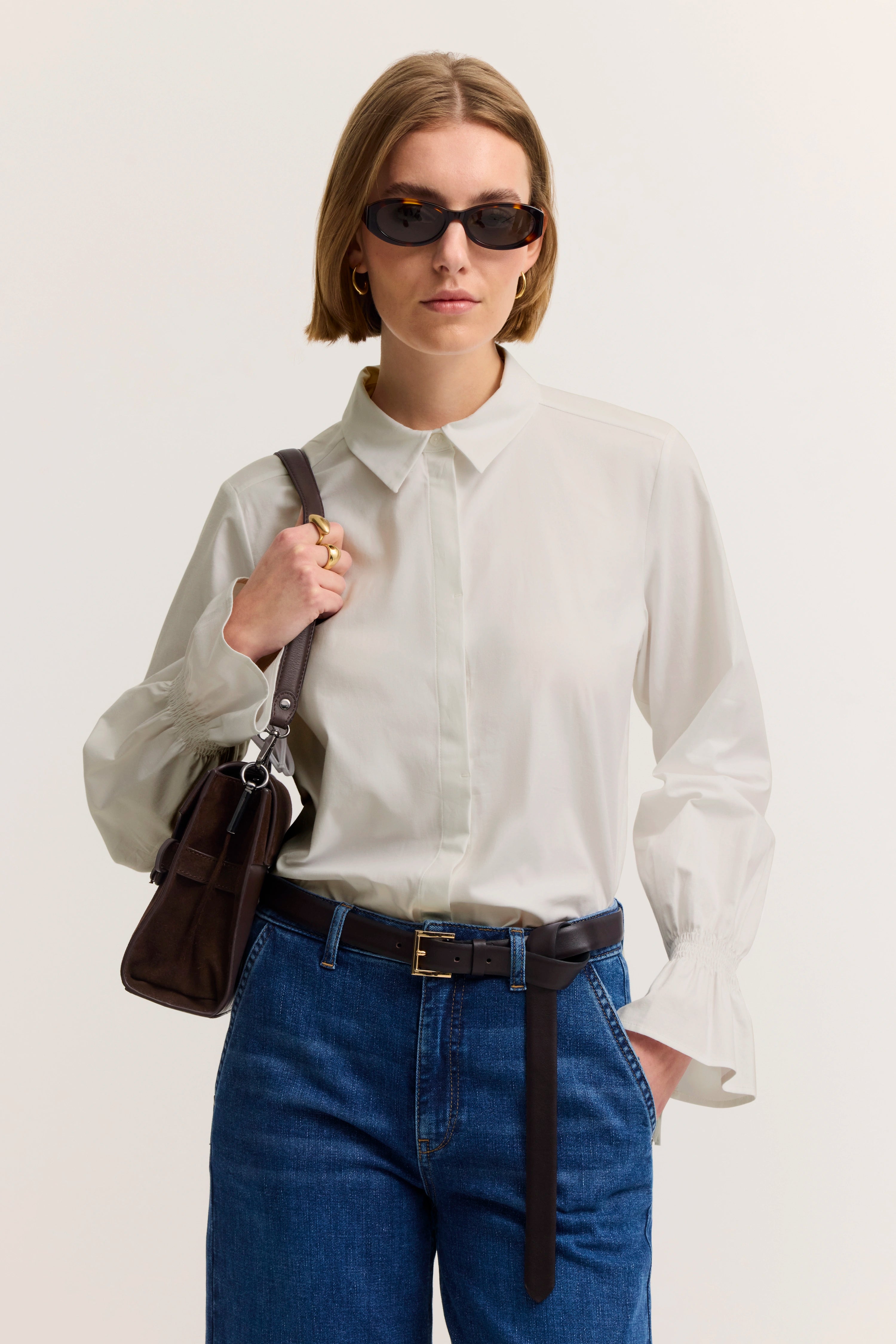Weiße Bluse und blaue Jeans, Modelbild mit Tasche, lässige Pose.