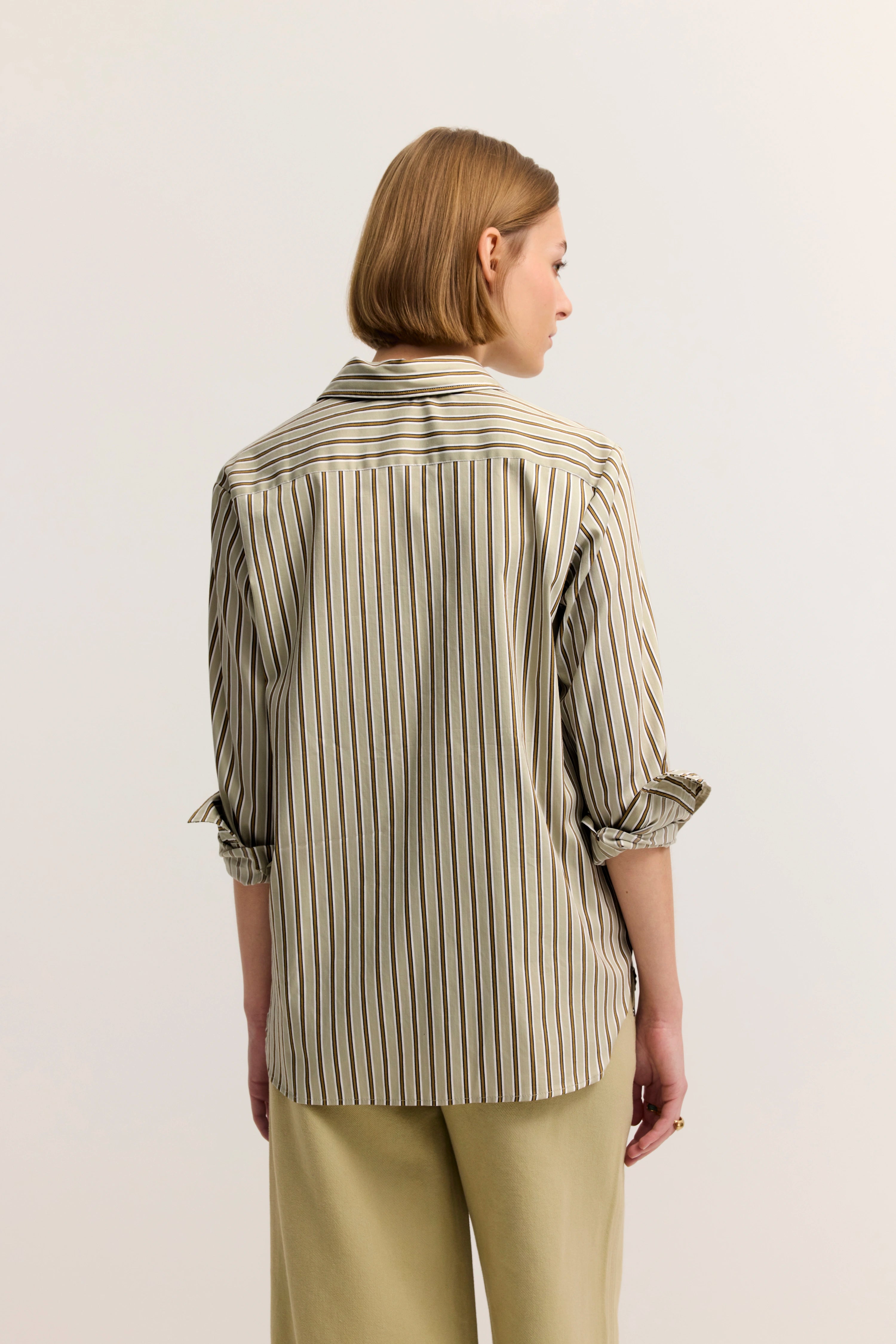 Modell in gestreiftem Hemd in Beige, lässig posierend, Rückansicht, Ärmel hochgekrempelt.