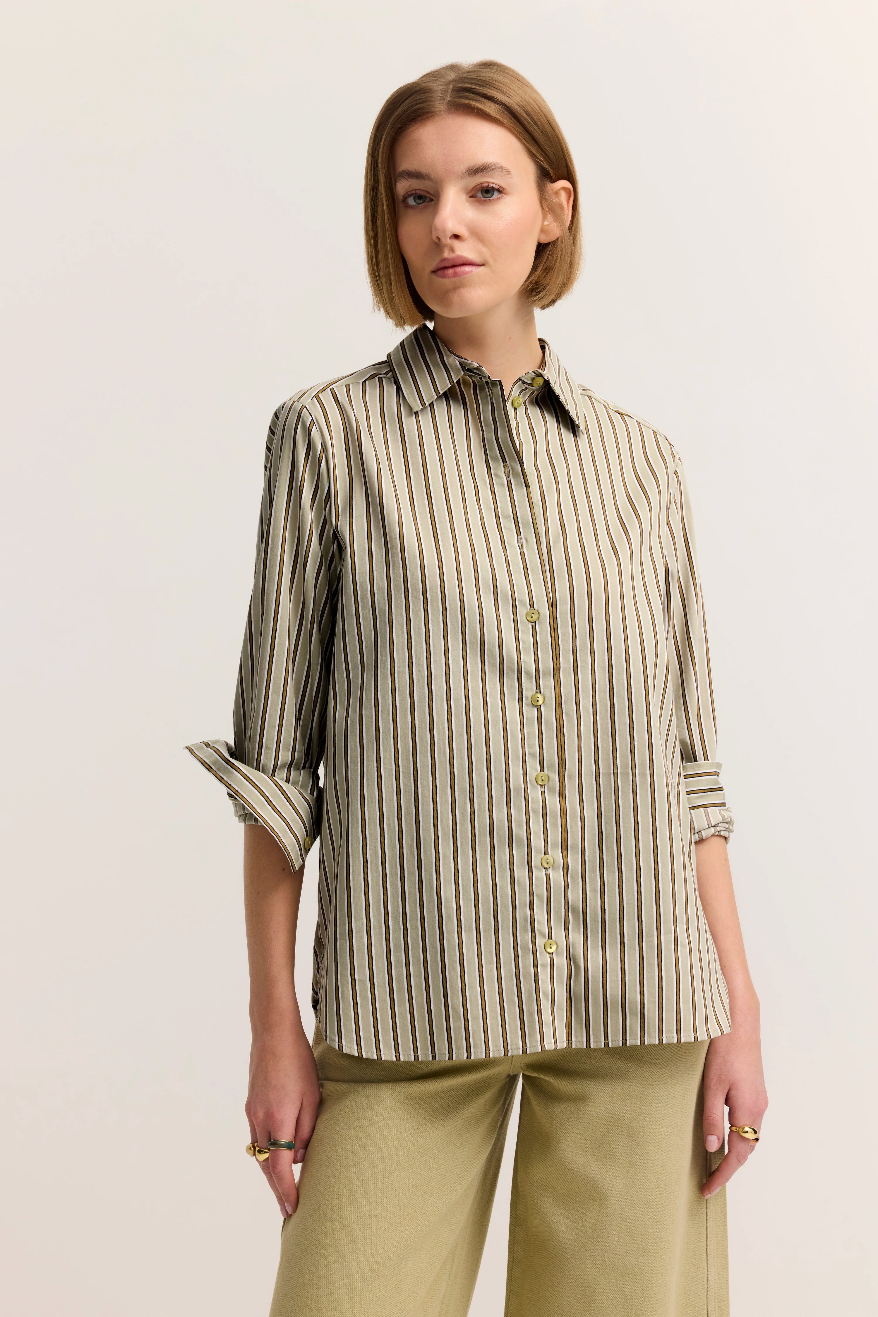 Gestreifte Bluse in Beige und Braun, Modelbild, lässig posierend, Ärmel hochgekrempelt.