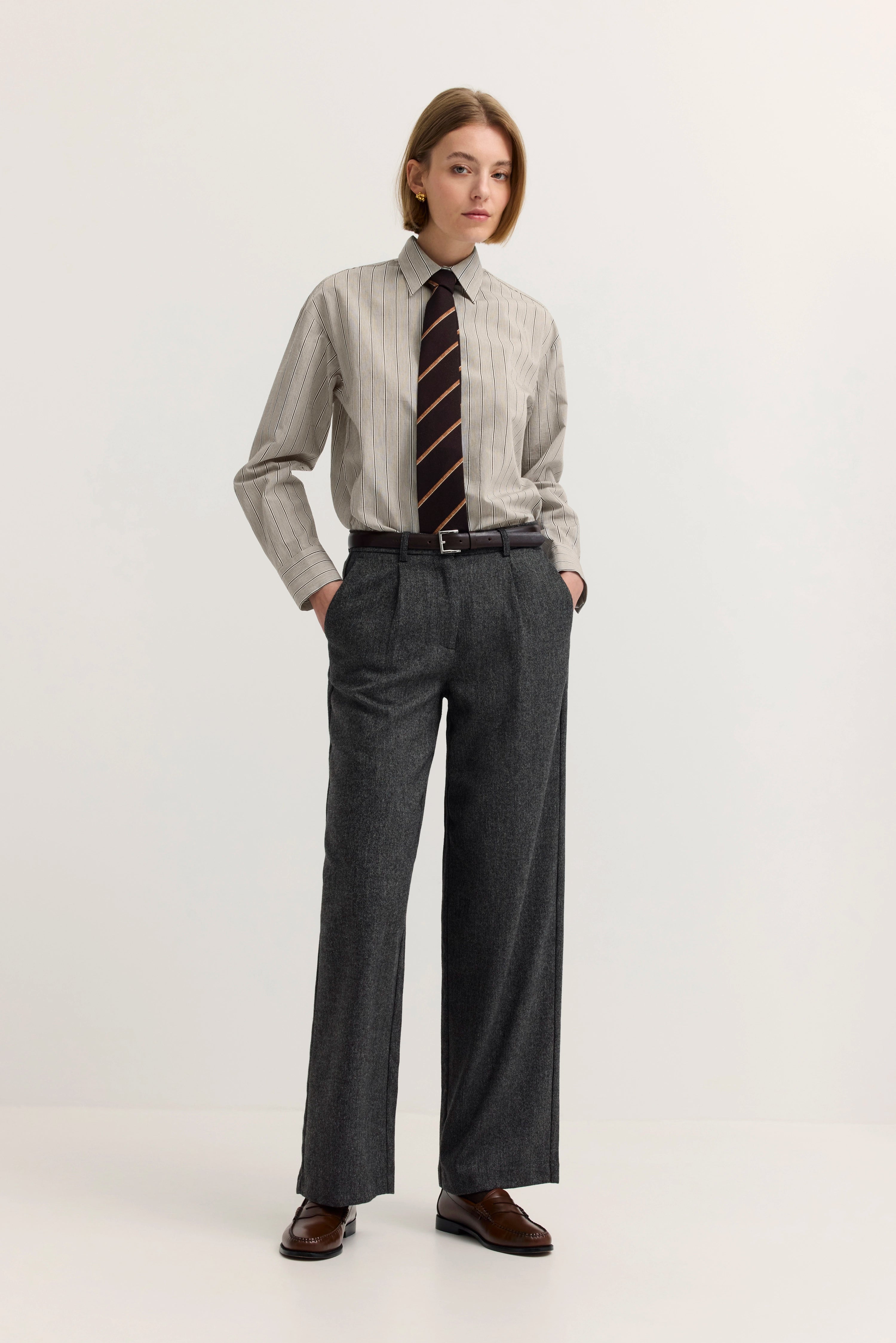 Graues Outfit mit Streifenhemd und Krawatte auf Model, Hände in Taschen, bugatti Stil.