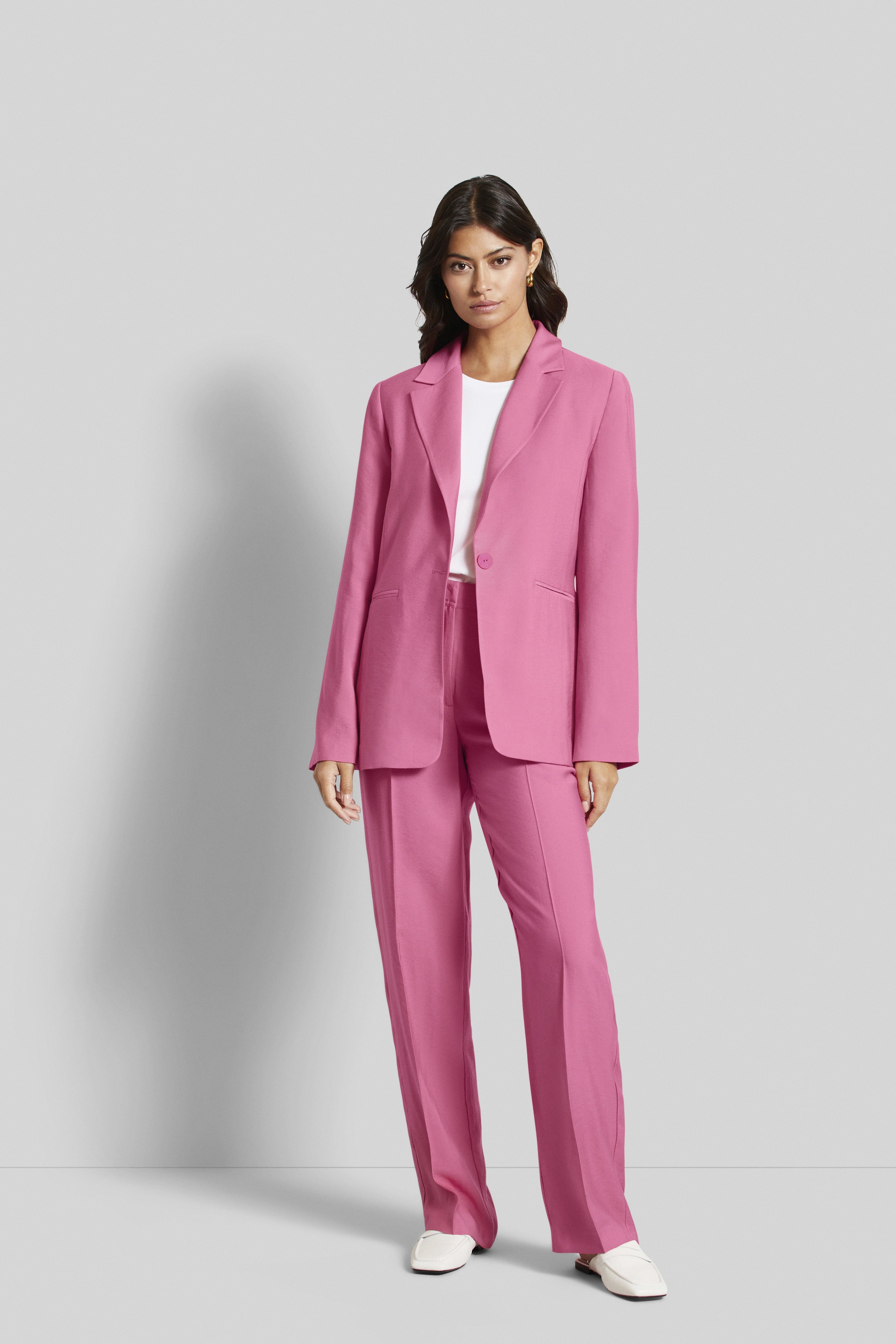 Model im rosa Anzug mit weißem Shirt, frontal stehend. Eleganz und Stil von bugatti.