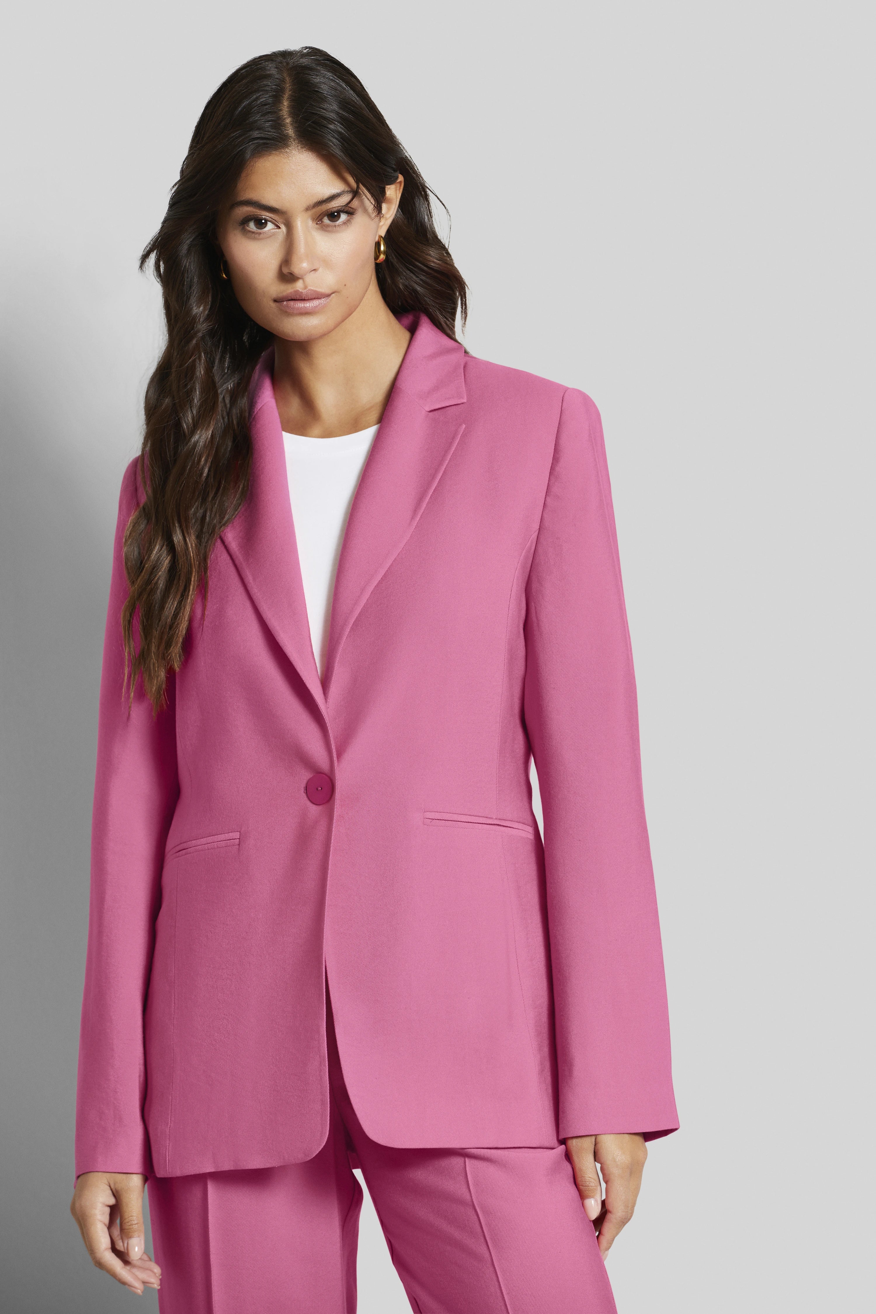 Model in roze blazer en broek van bugatti, wit shirt, ontspannen pose.