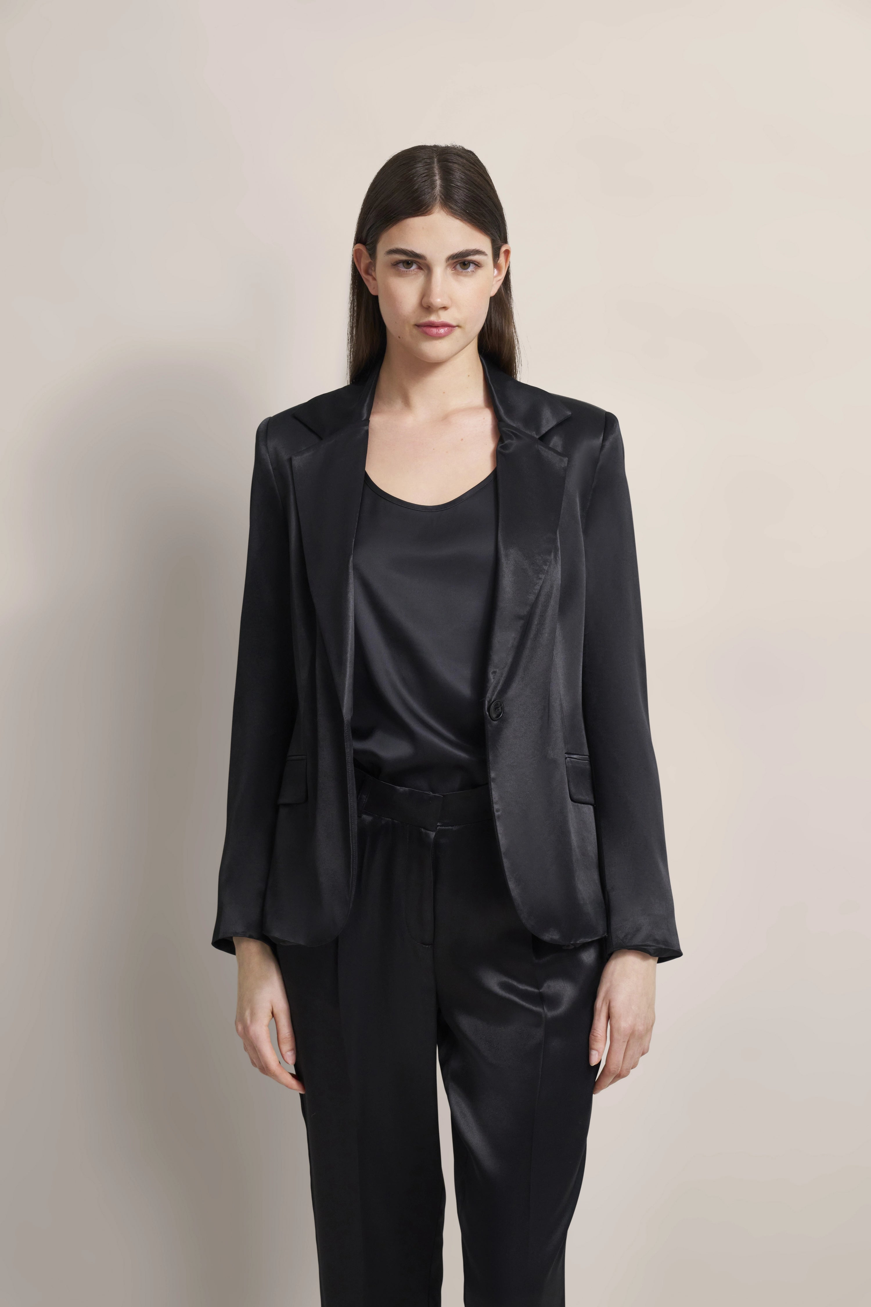 Model draagt zwart satijnen outfit: blazer, top en broek. Klassiek, elegant poseren.