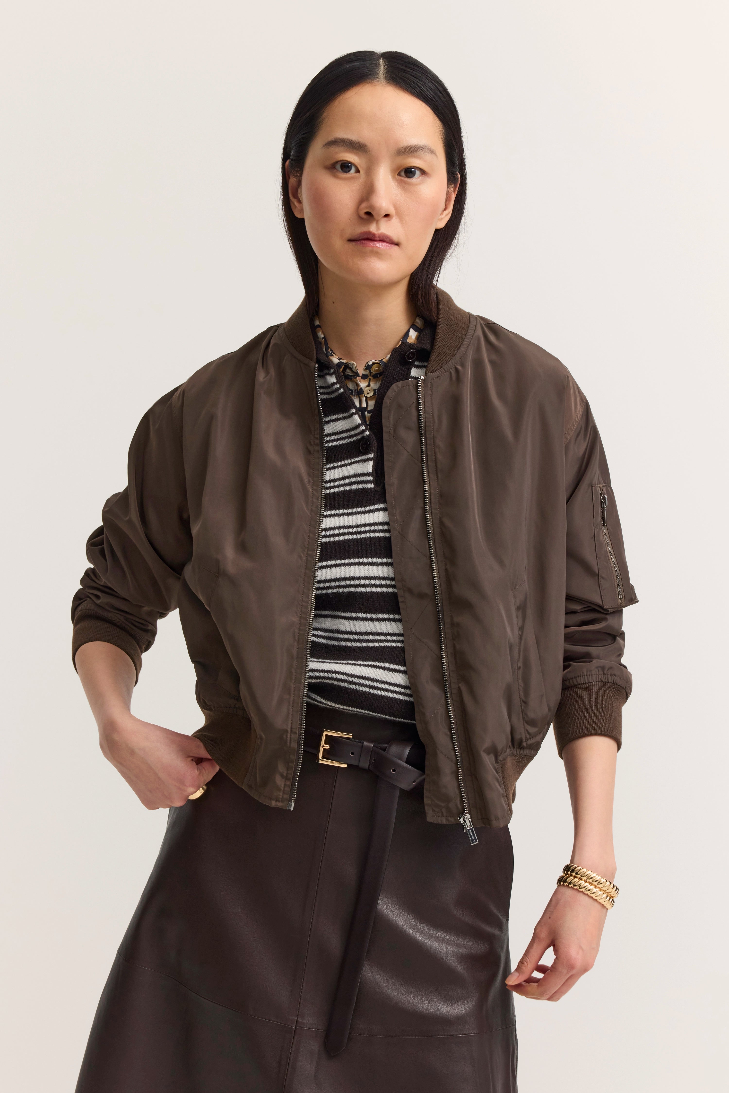 bugatti Modelbild: Braune Bomberjacke, gestreiftes Shirt, brauner Lederrock, lässige Pose.