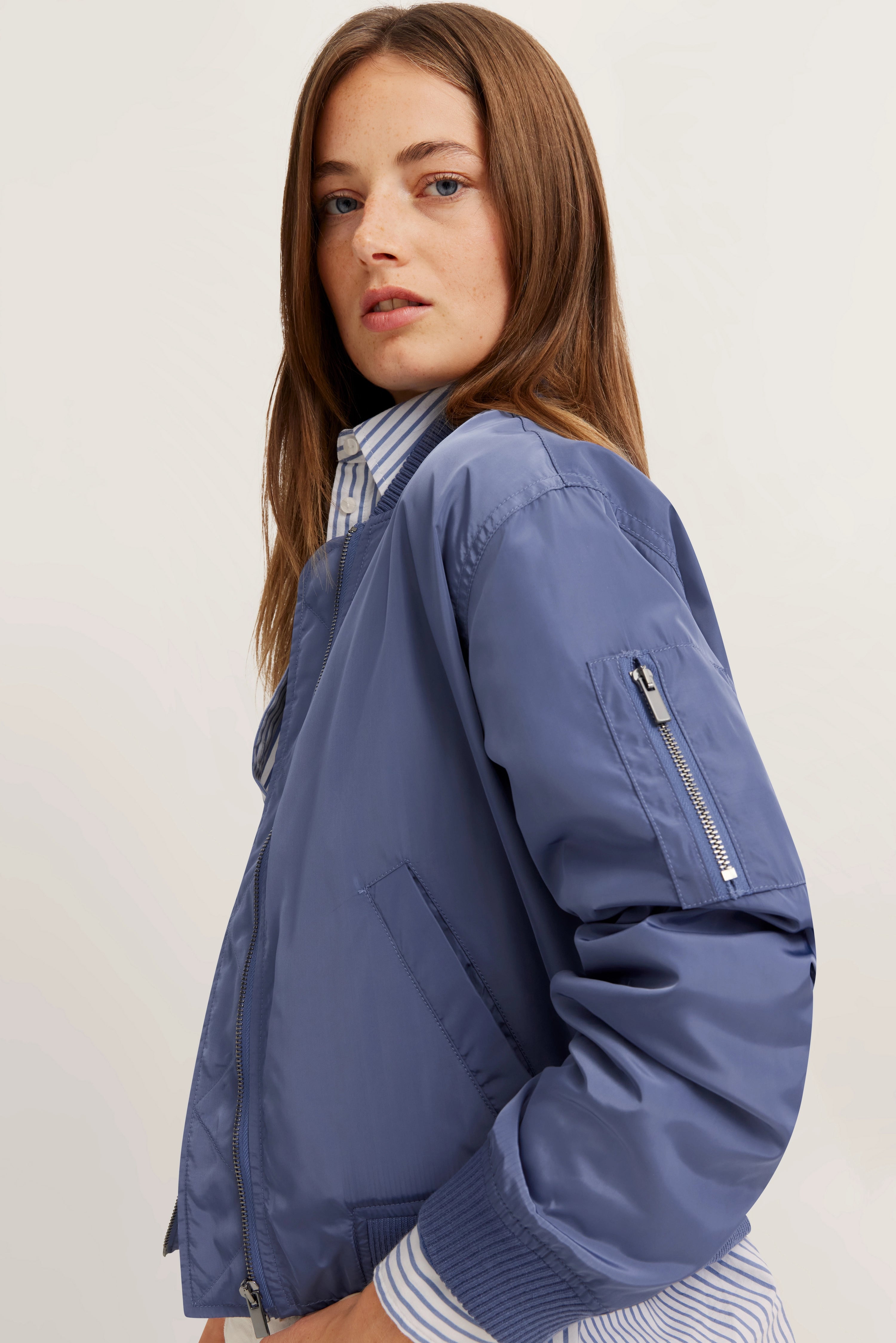 Model trägt blaue bugatti Bomberjacke über gestreifter Bluse, seitliches Posing.
