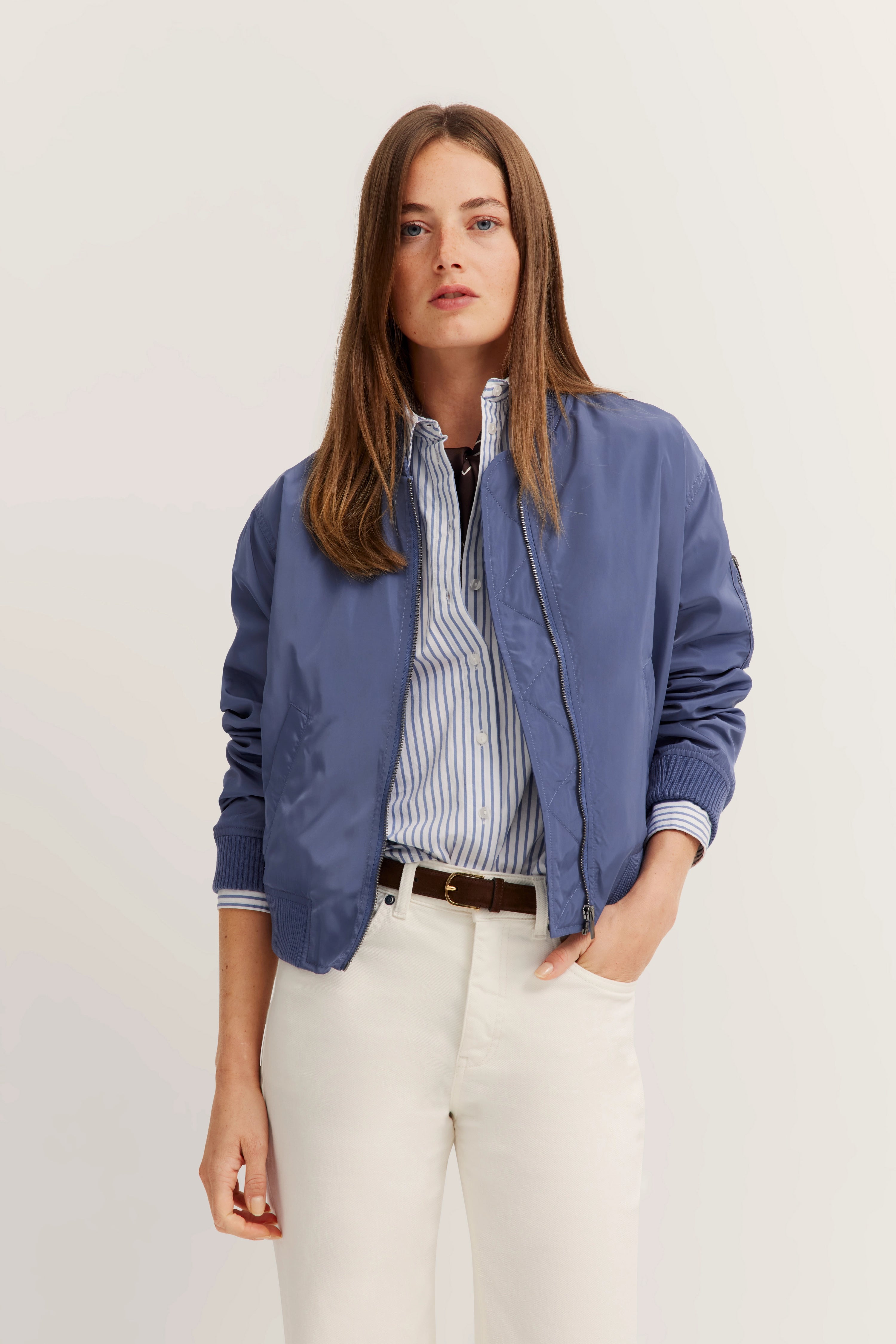 Model in blauer bugatti Jacke, gestreiftem Hemd und weißen Hosen, legeres Posing.