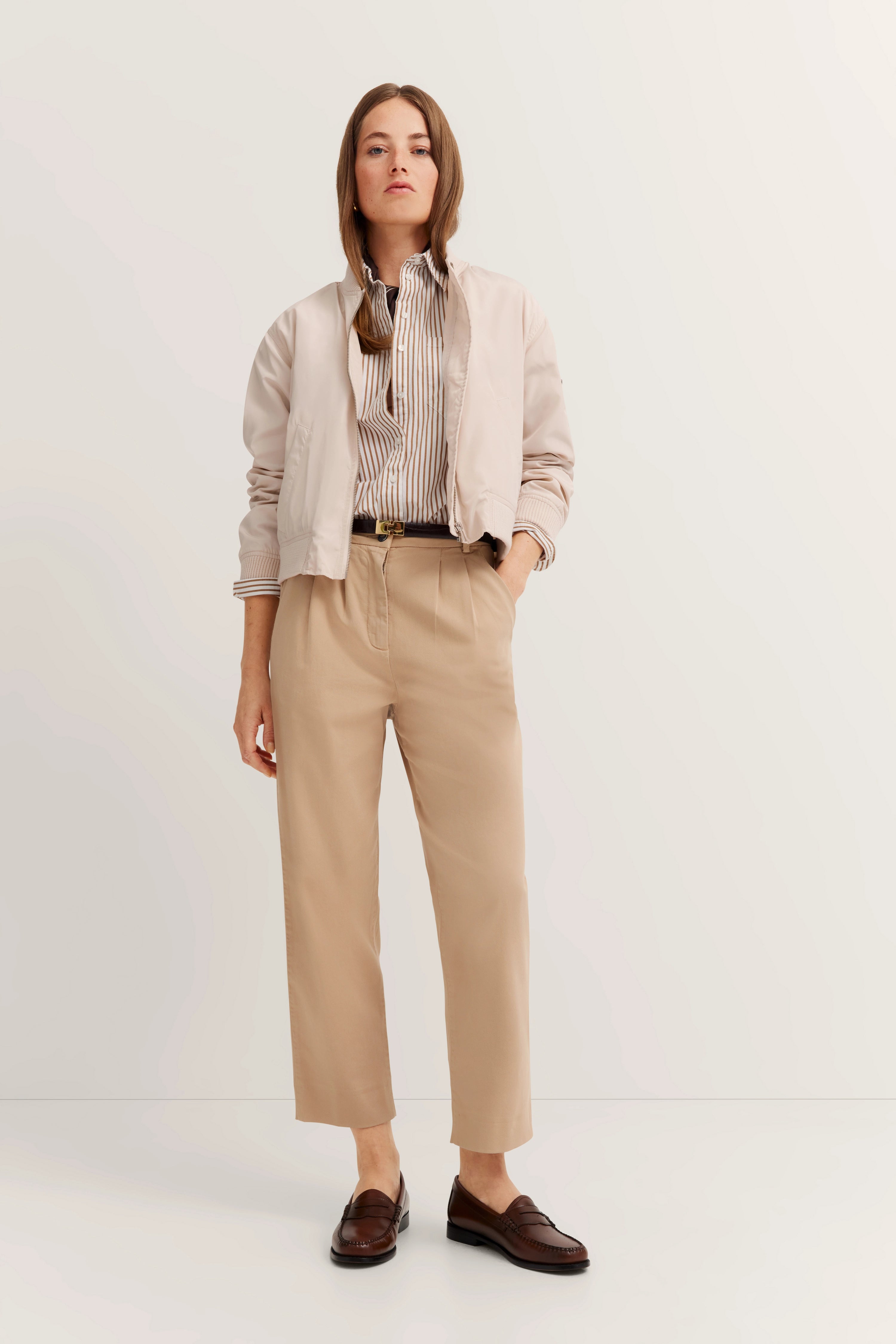 Beiger Blouson, gestreiftes Hemd, beige Hose, braune Loafer, Model stehend, bugatti Stil.