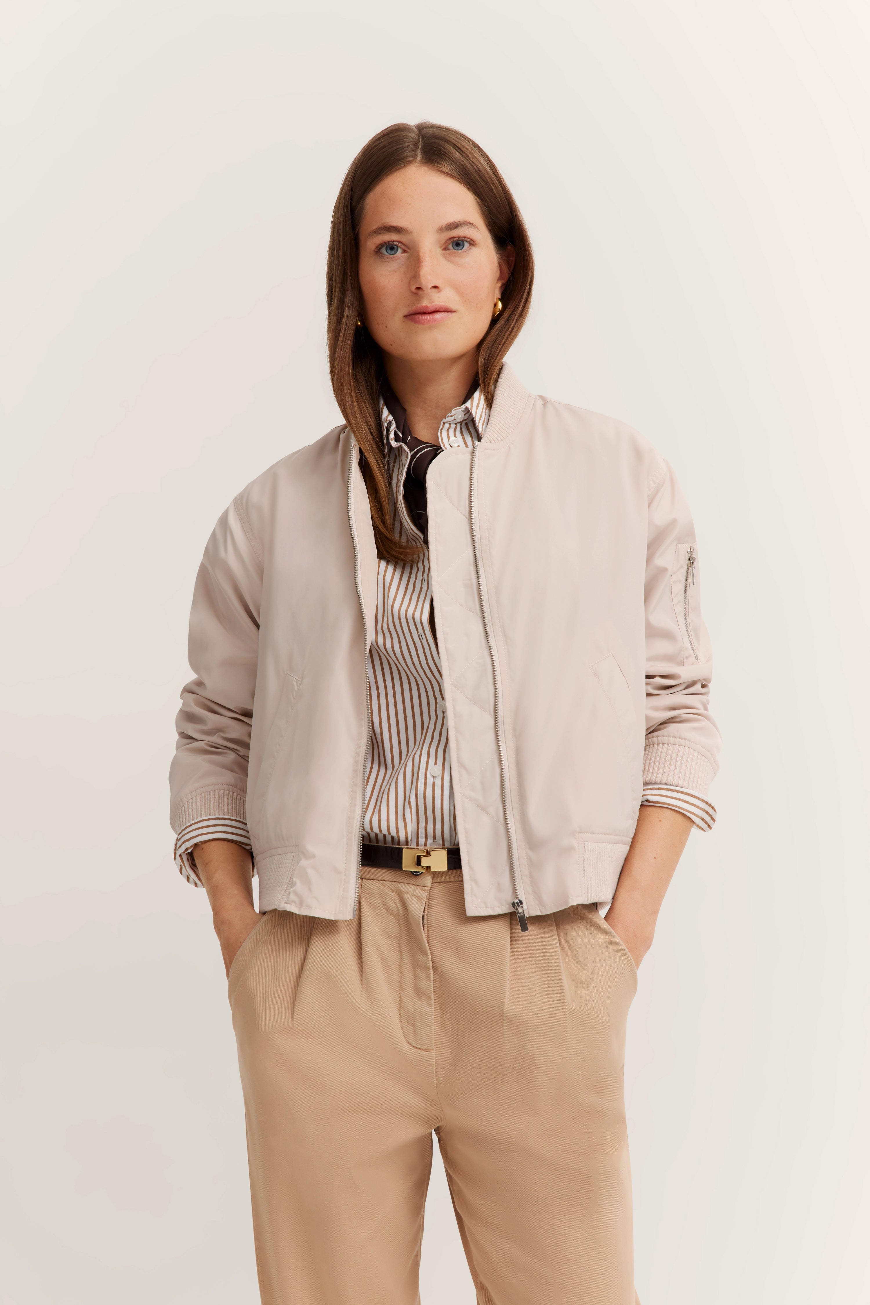 Model in hellbeiger Jacke und gestreiftem Hemd, beige Hose, entspannte Pose, bugatti Stil.