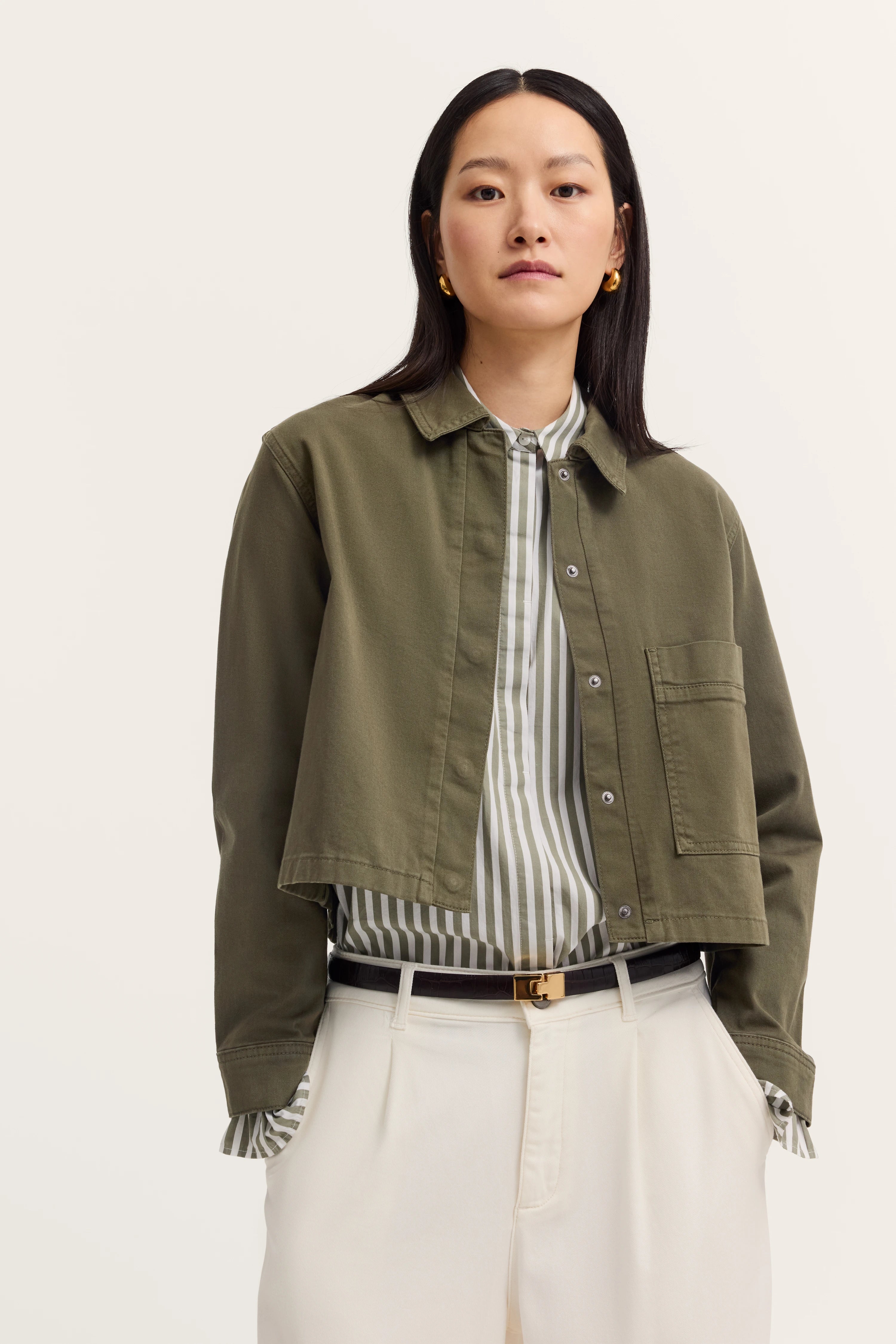 Groen shirt en gestreepte blouse met witte broek, casual model, handen in zakken.