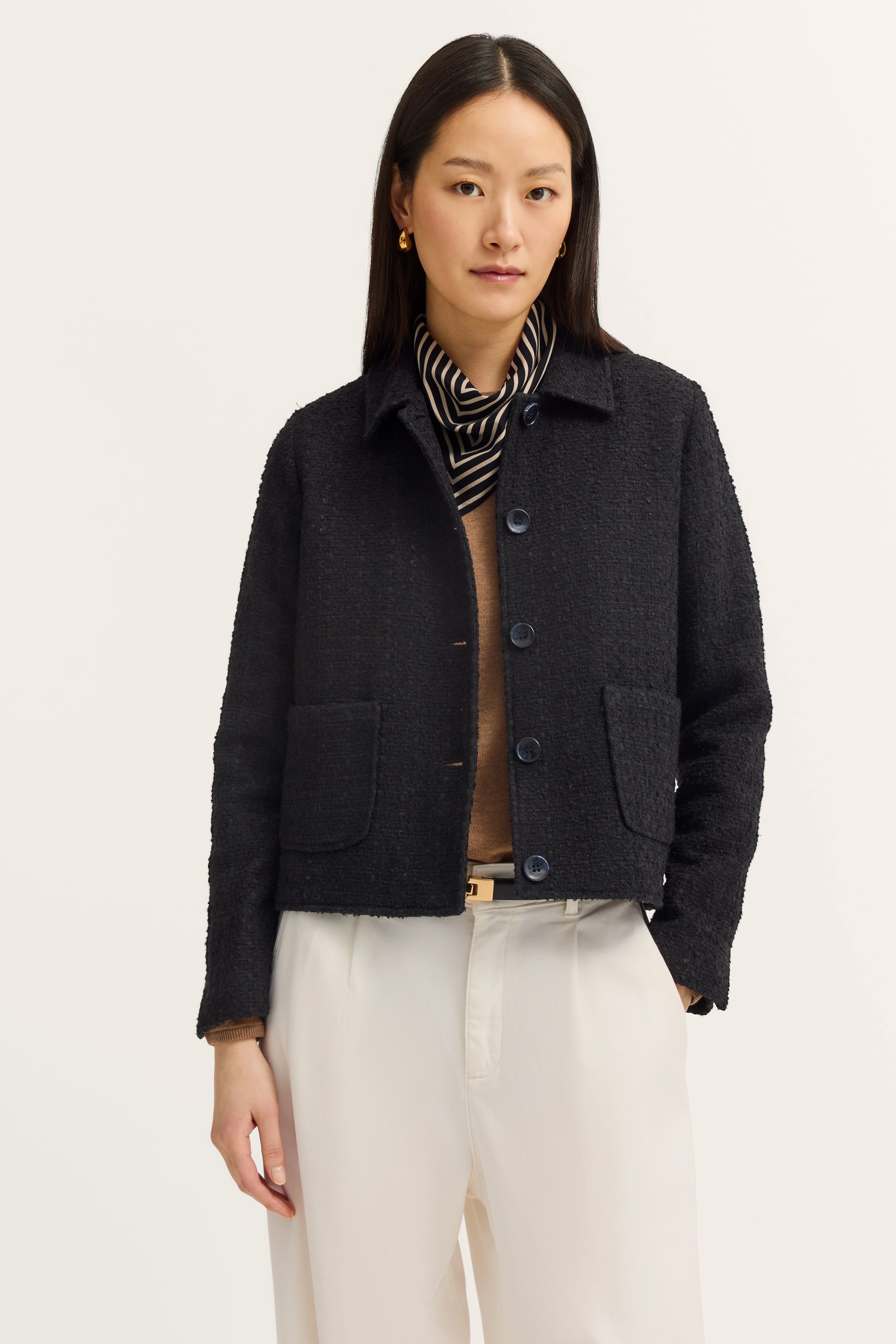 Model draagt zwarte bugatti blazer, gestreepte sjaal, beige top en witte broek.
