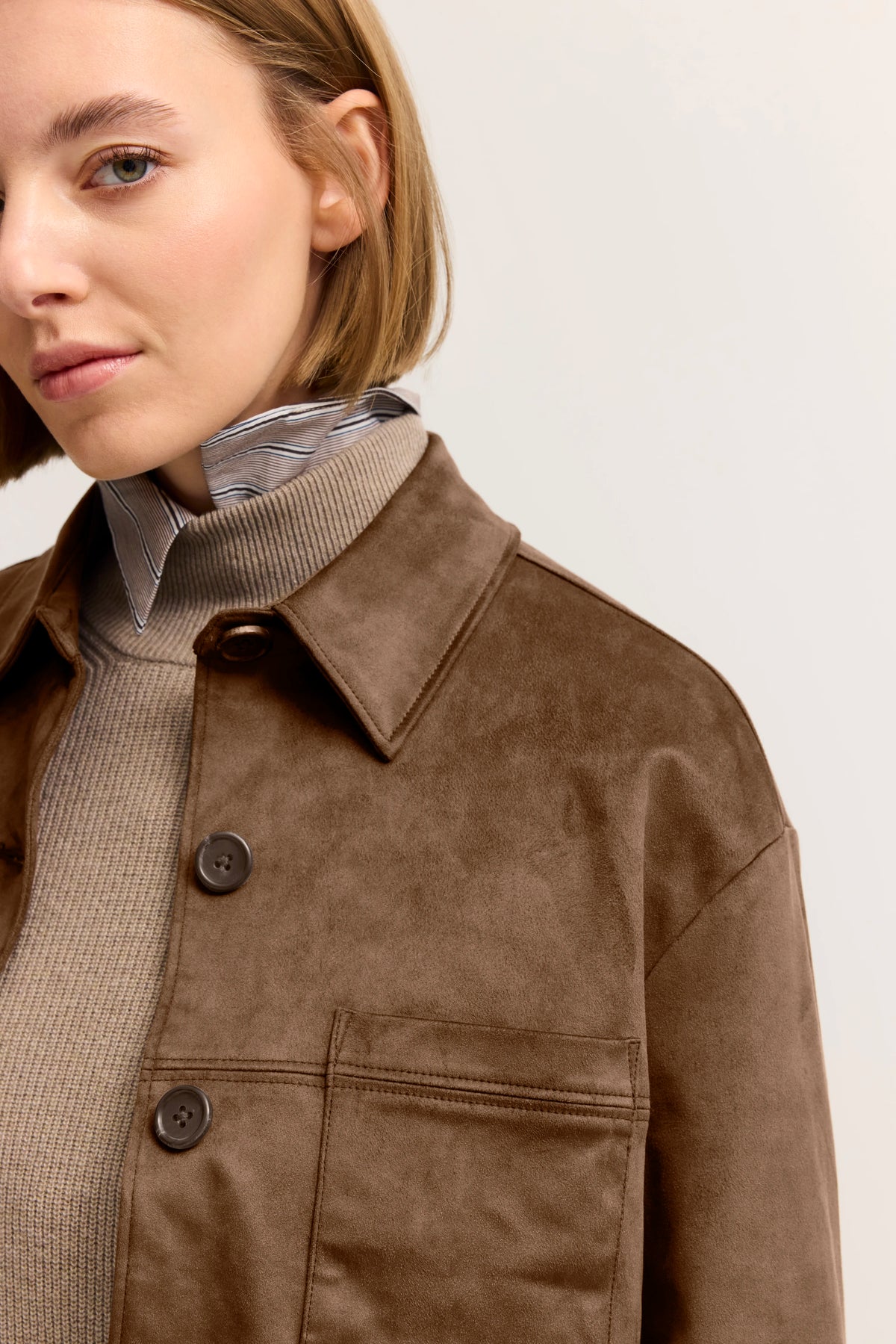 Braune Jacke und gestreiftes Hemd im Modelbild, halb seitlich, elegantes Profil.