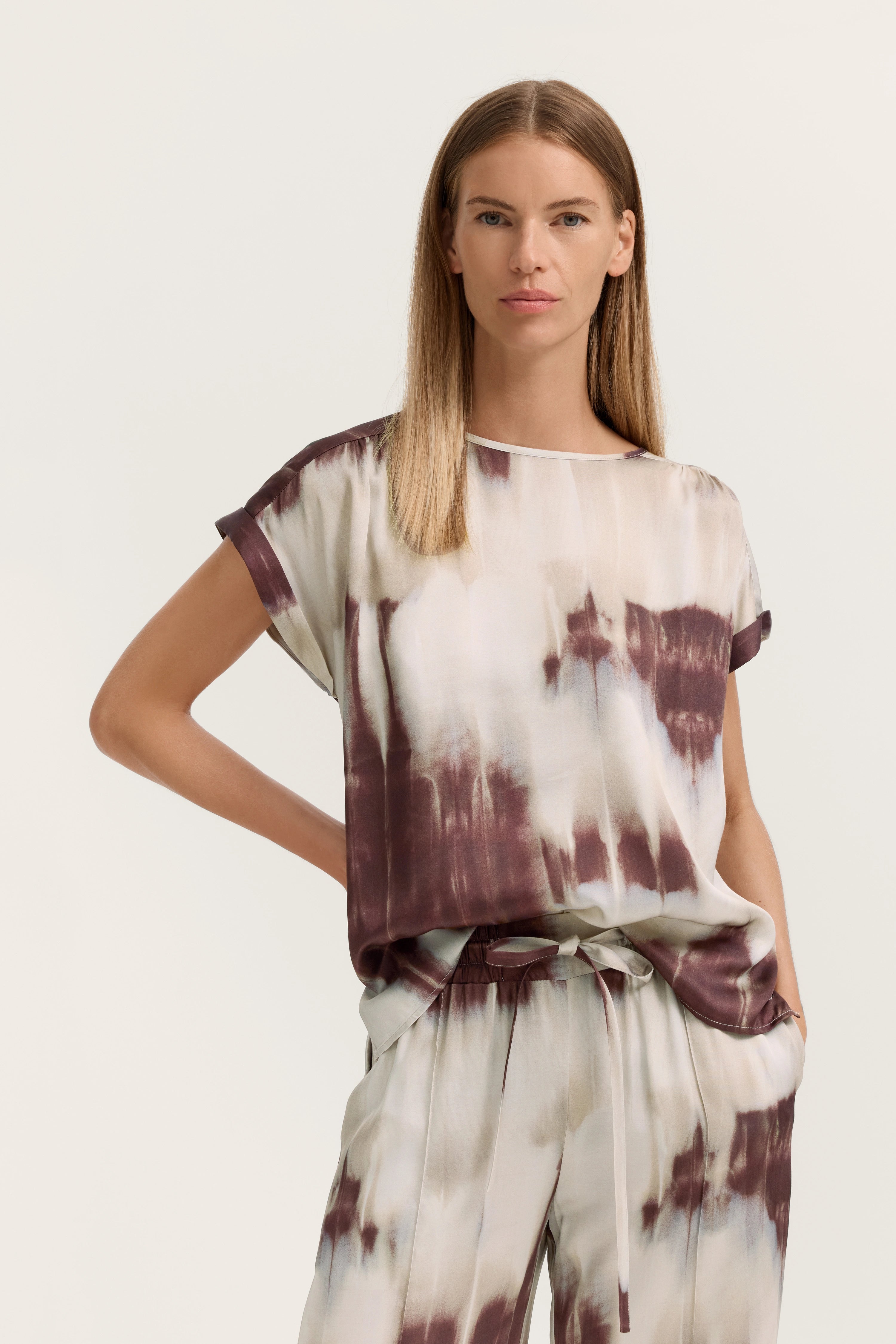 Model in legerem bugatti Outfit, Batikmuster Oberteil und Hose, entspannte Pose, italienische Gelassenheit.