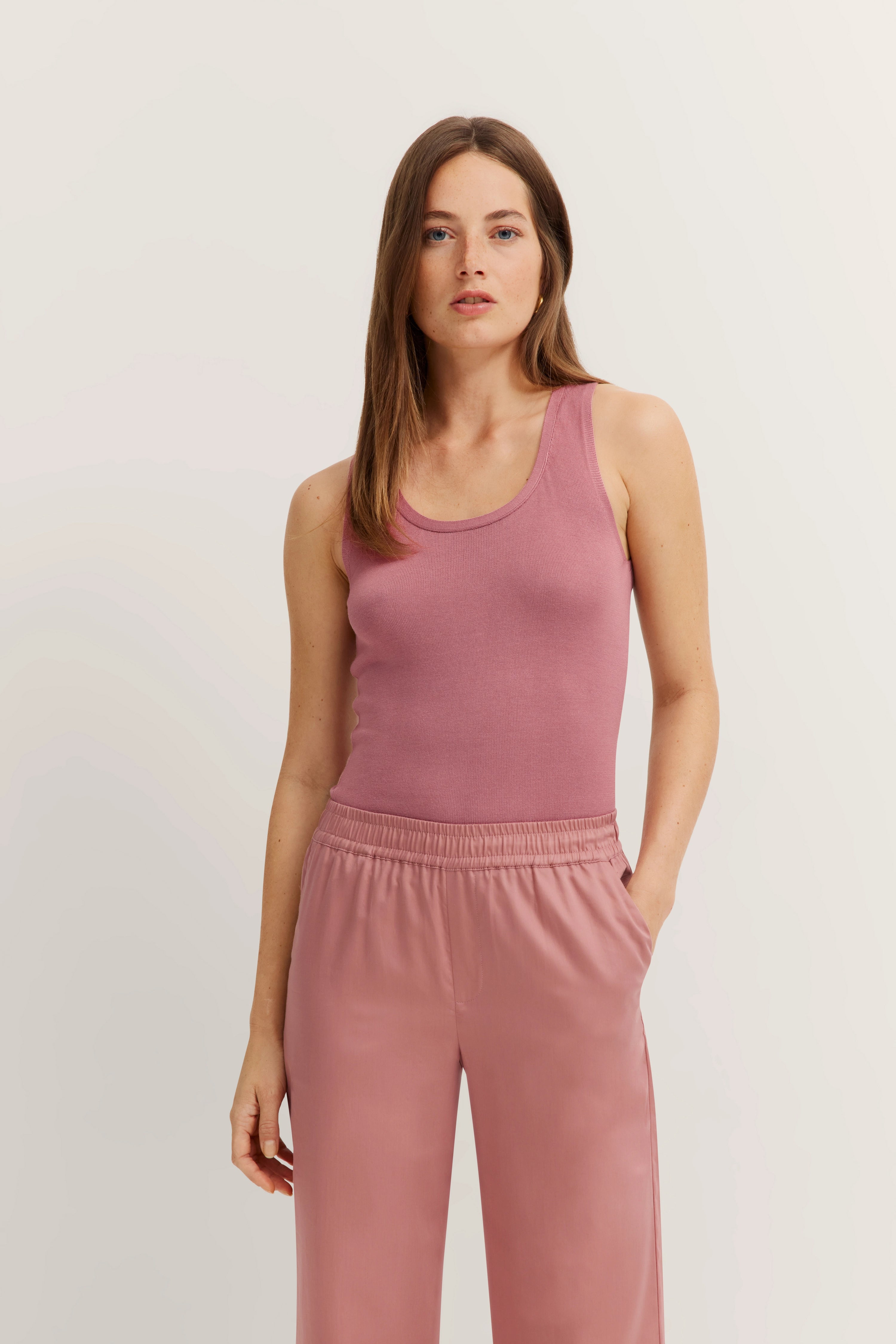 Model draagt een roze mouwloos topje met bijpassende broek, in ontspannen houding.