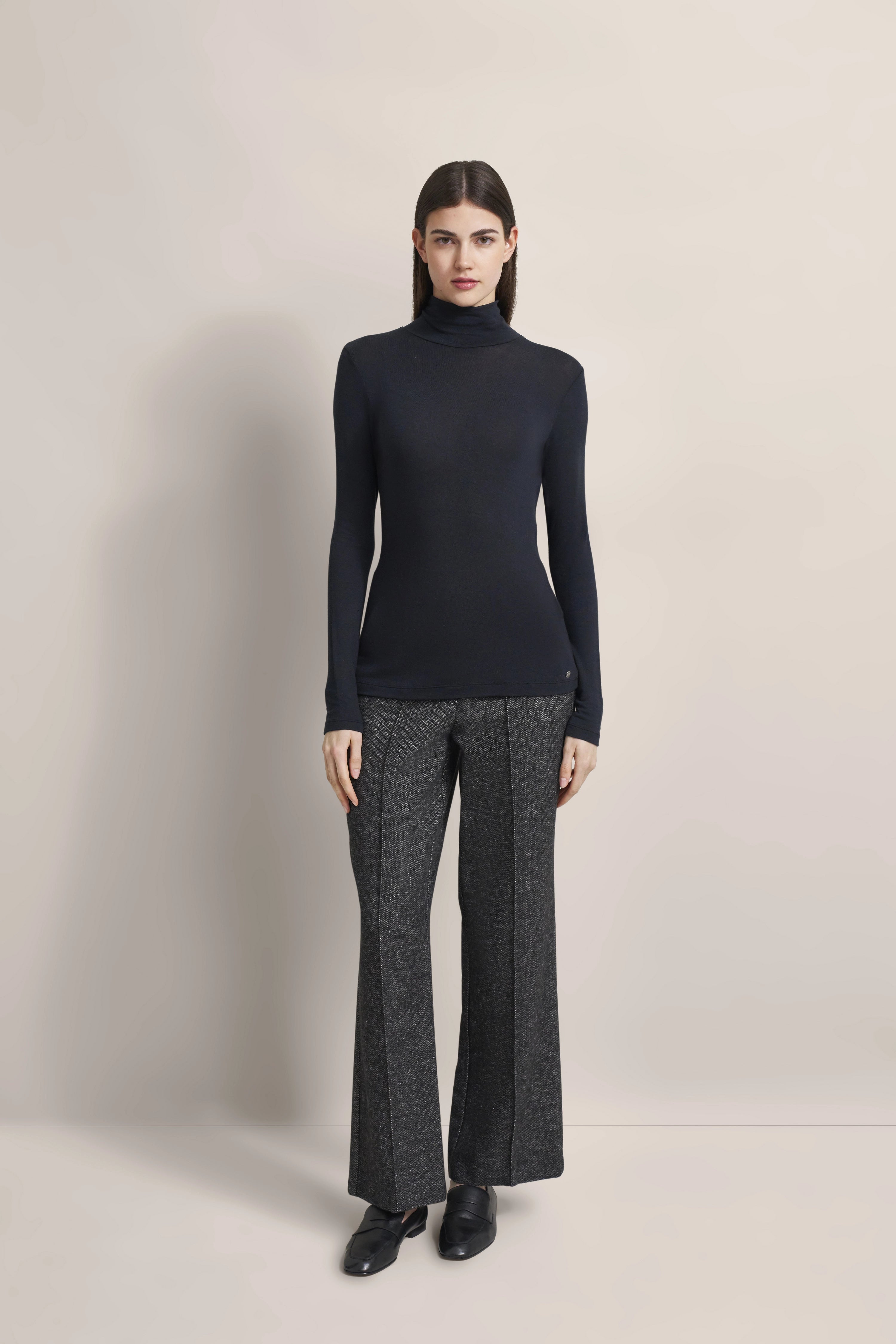 Model in schwarzem Rollkragenpullover und grauer Hose von bugatti, stehend, entspannte Pose.