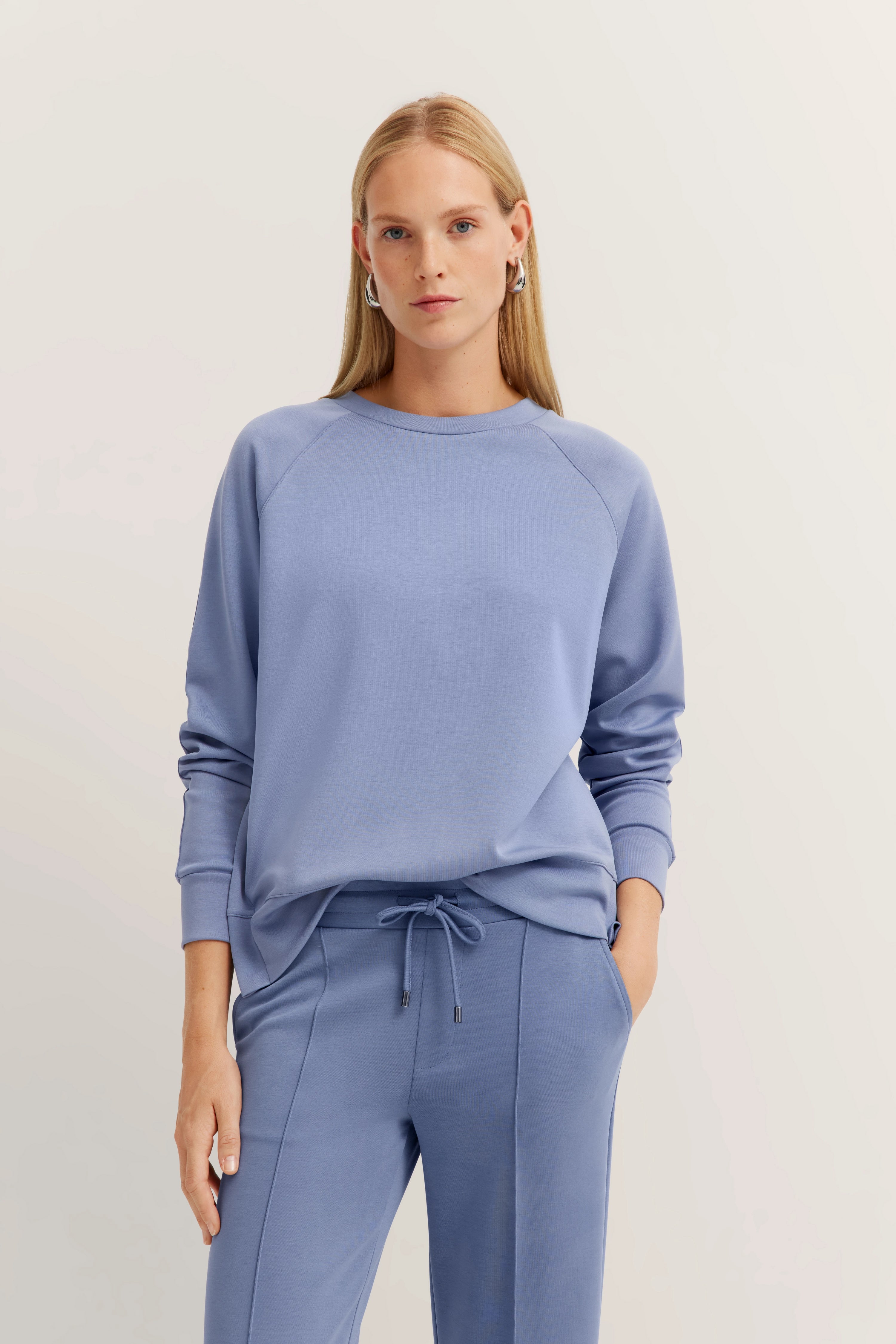 Model in ontspannen look met lichtblauwe bugatti sweatshirt en joggingbroek, handen in de zakken.