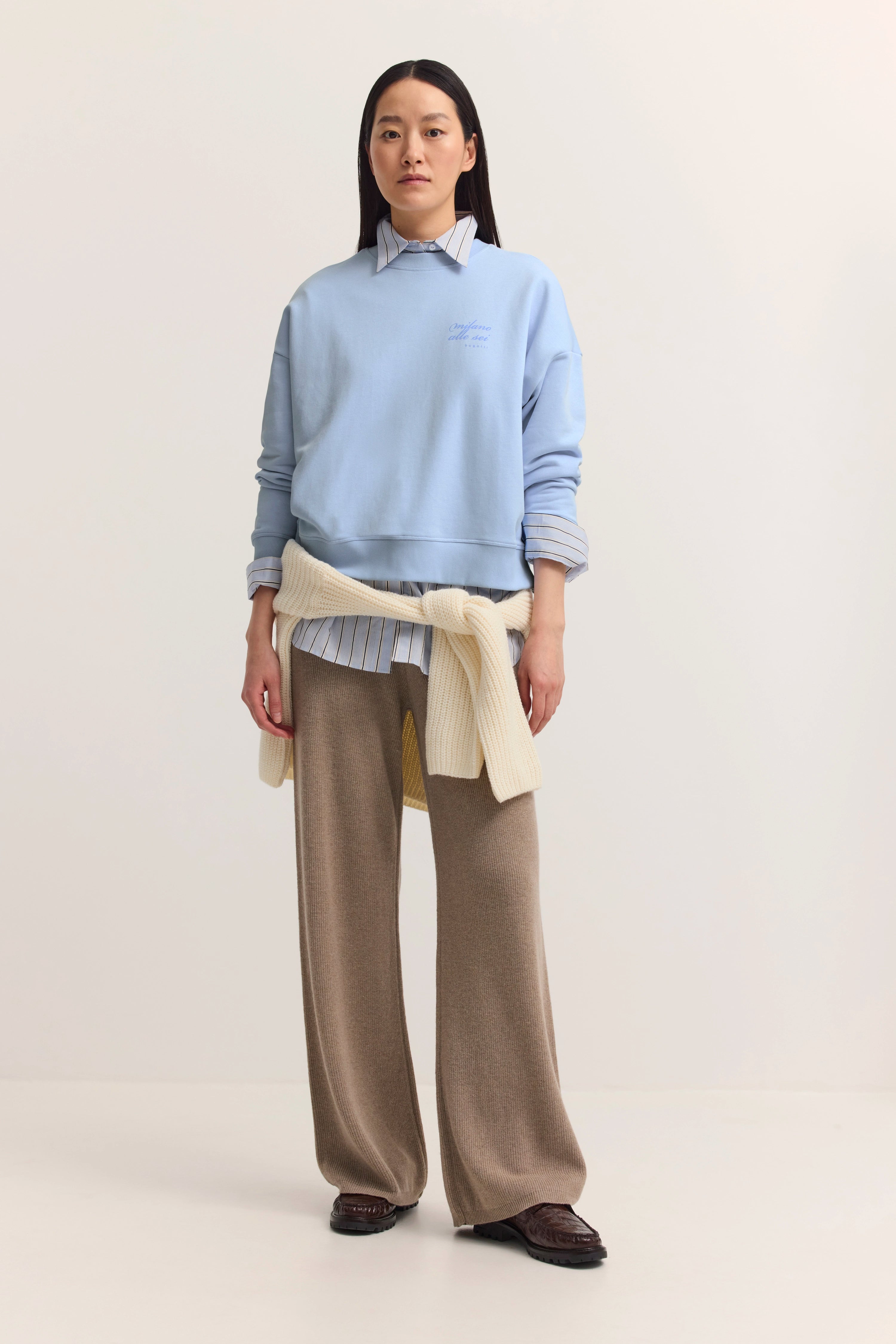 Elegantes Model in blauem Pullover, beige Hose, Hemd und Strickjacke von bugatti, entspanntes Posing.