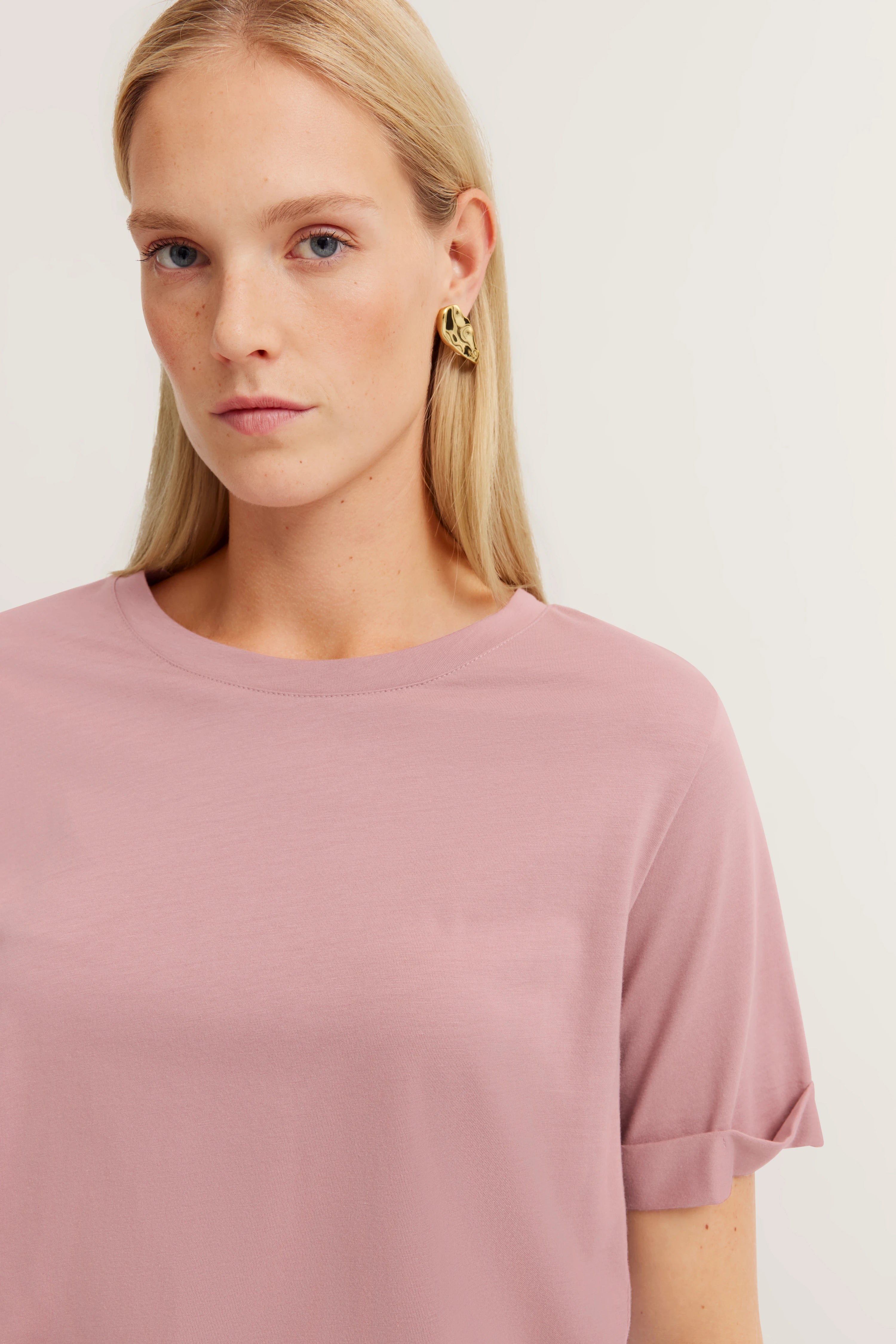 Model met roze bugatti T-shirt, casual pose, gouden oorbellen.