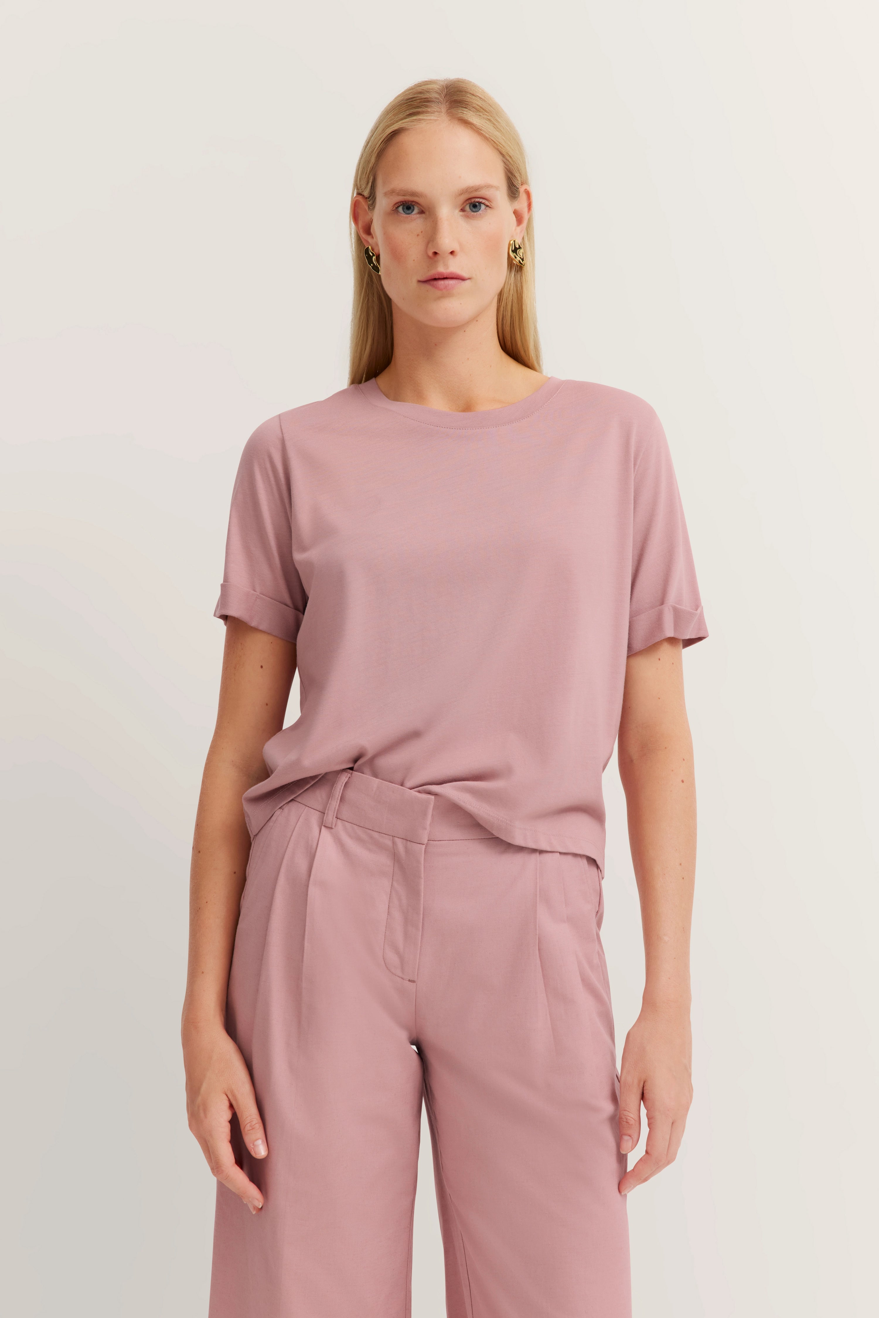 Model draagt oudroze T-shirt en broek van bugatti. Ontspannen pose, rustige uitstraling.